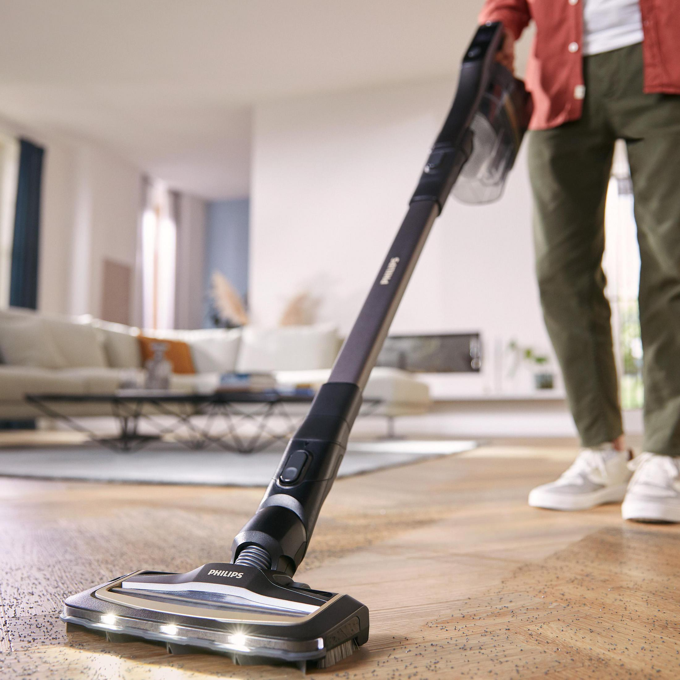 Person saugt Holzboden mit Akku-Staubsauger, im Hintergrund Wohnzimmer.