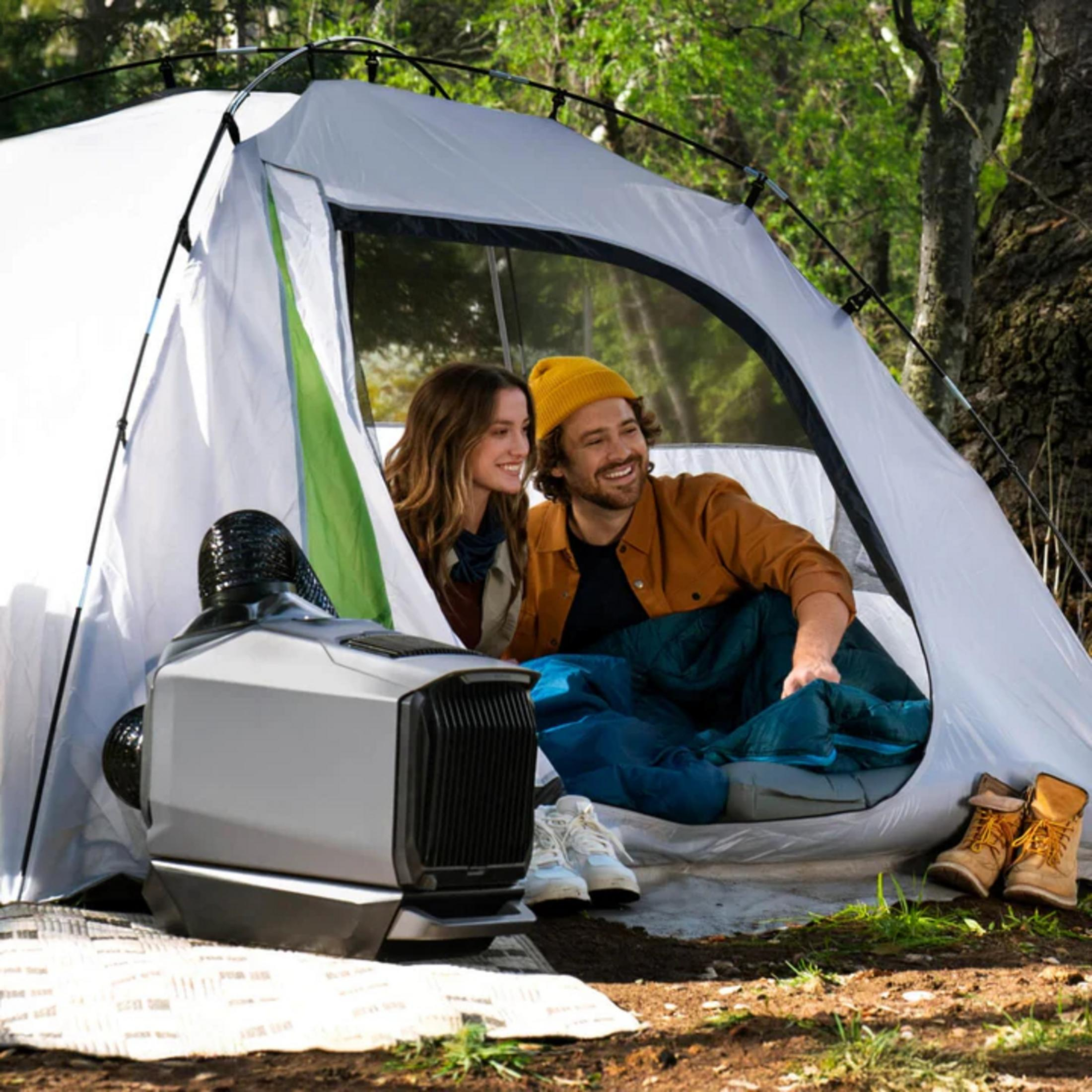 Para śmieje się w namiocie z przenośną jednostką klimatyzacyjną na zewnątrz.