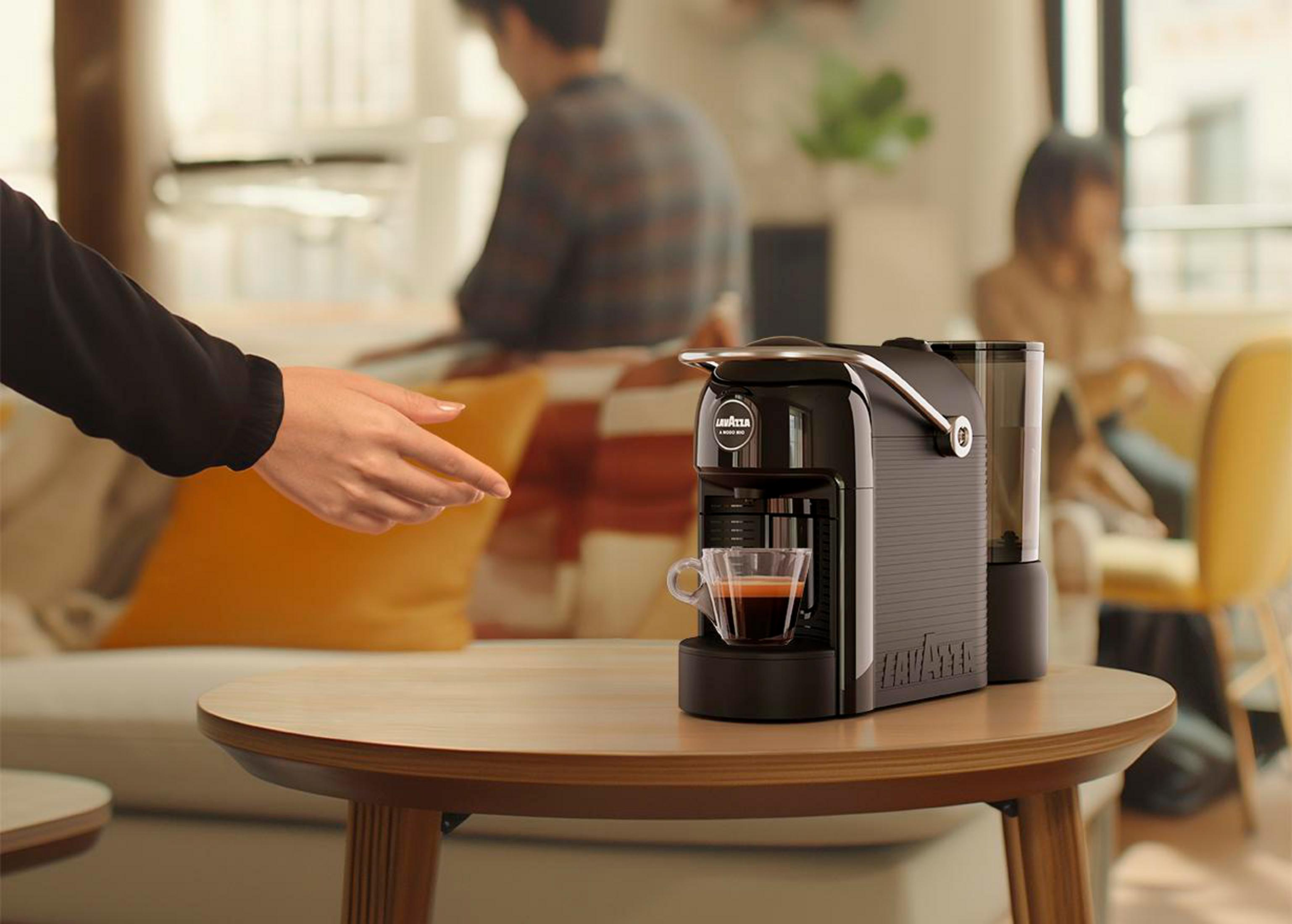 Eine schwarze Kaffeemaschine auf einem Holztisch mit einer Tasse Espresso.