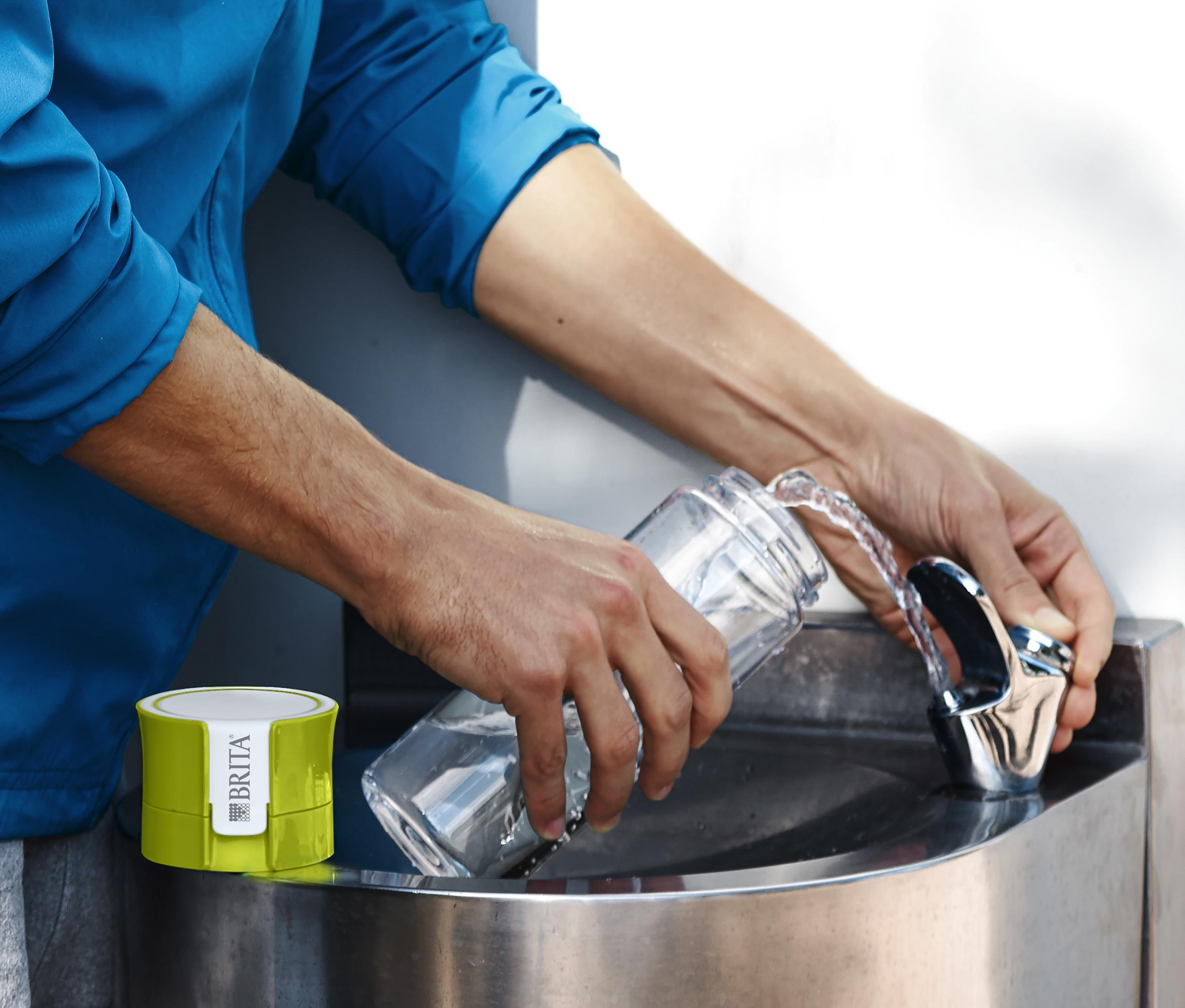 Persoon vult een fles bij een waterfontein met groen BRITA-filter.