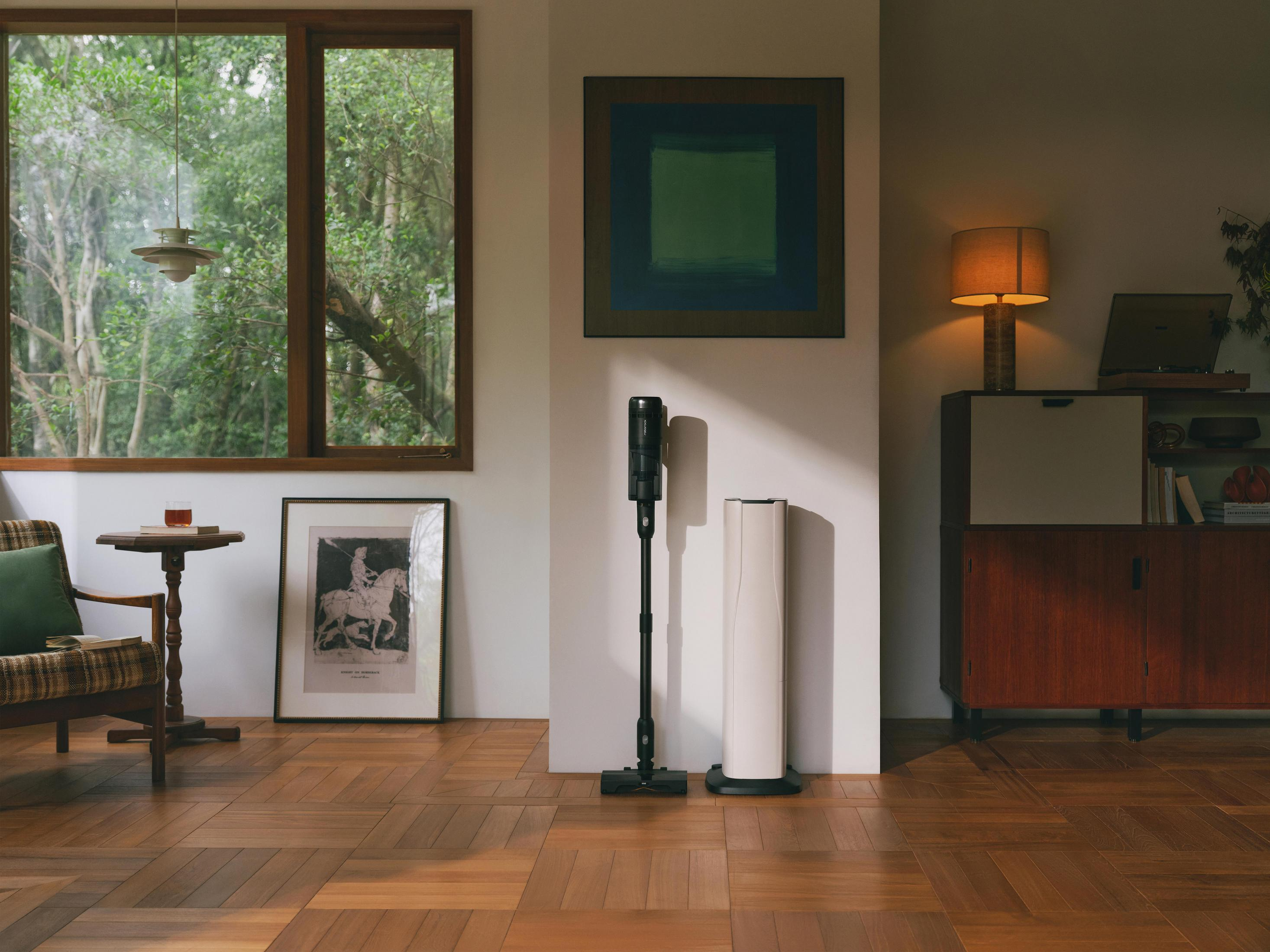 Un soggiorno con parquet, poltrona, cornice, aspirapolvere e lampada.