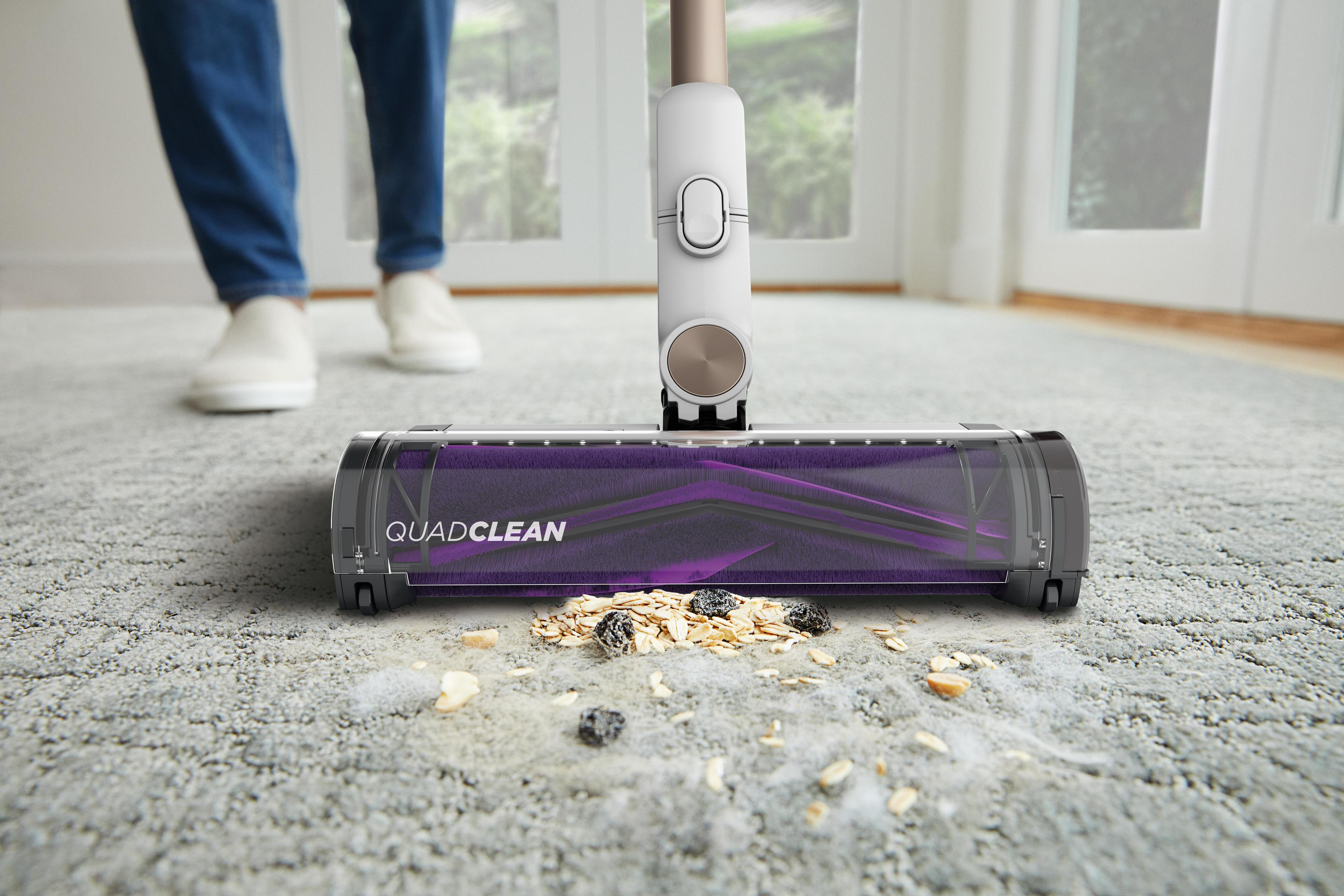 Una aspiradora con cepillo morado recoge migas en una alfombra clara.