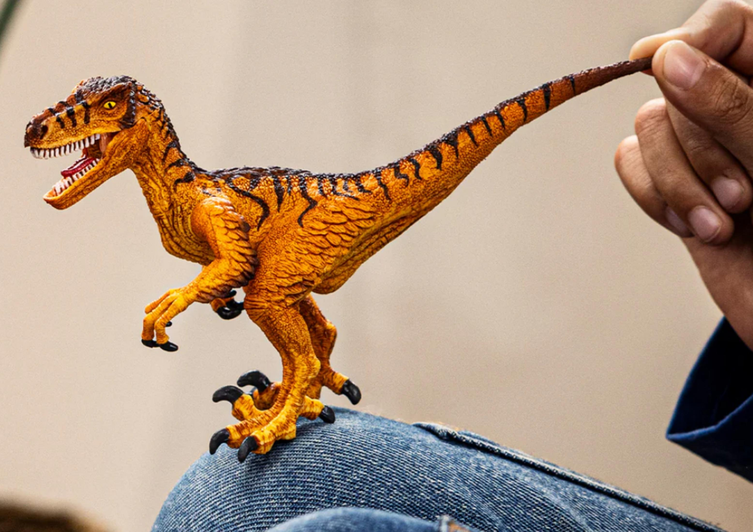 Oranje Velociraptor figuur met zwarte strepen vastgehouden door een hand.