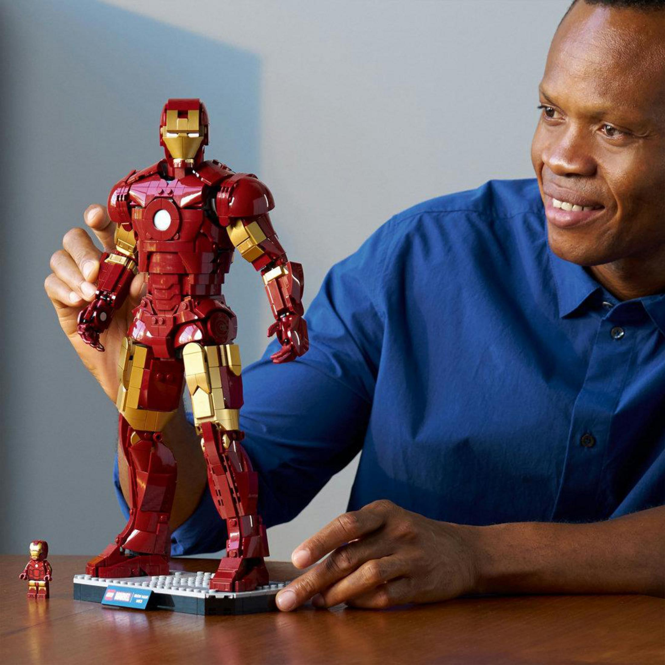 Mavi gömlekli bir adam, büyük kırmızı ve altın renkli Lego Iron Man figürüne bakıyor.