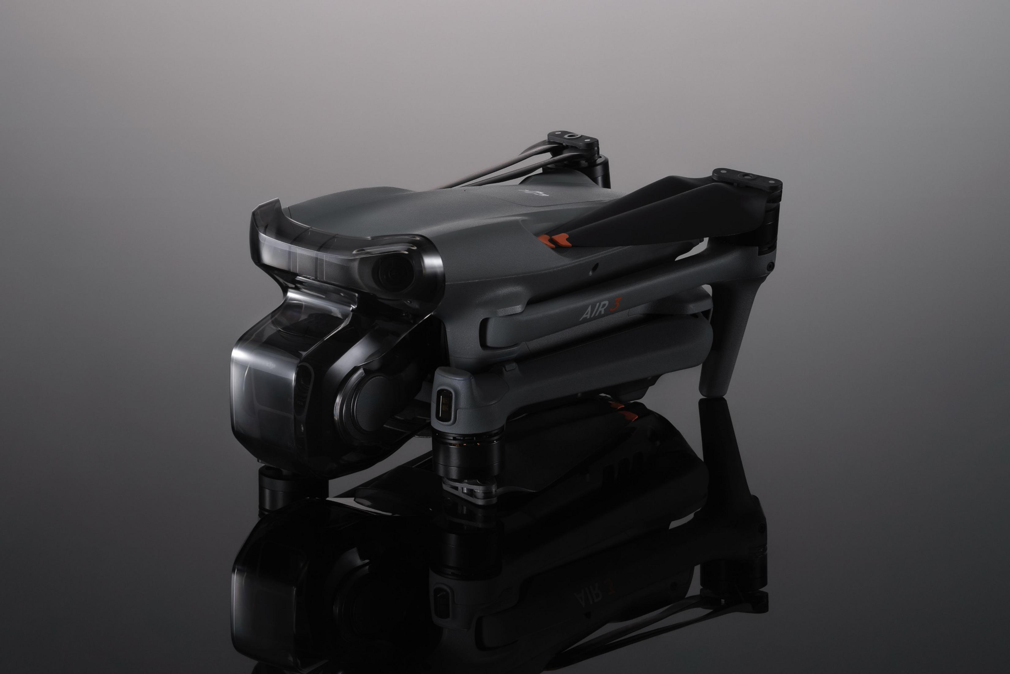 Drone DJI Air 3 grigio pieghevole con telecamere ed eliche su una superficie riflettente.