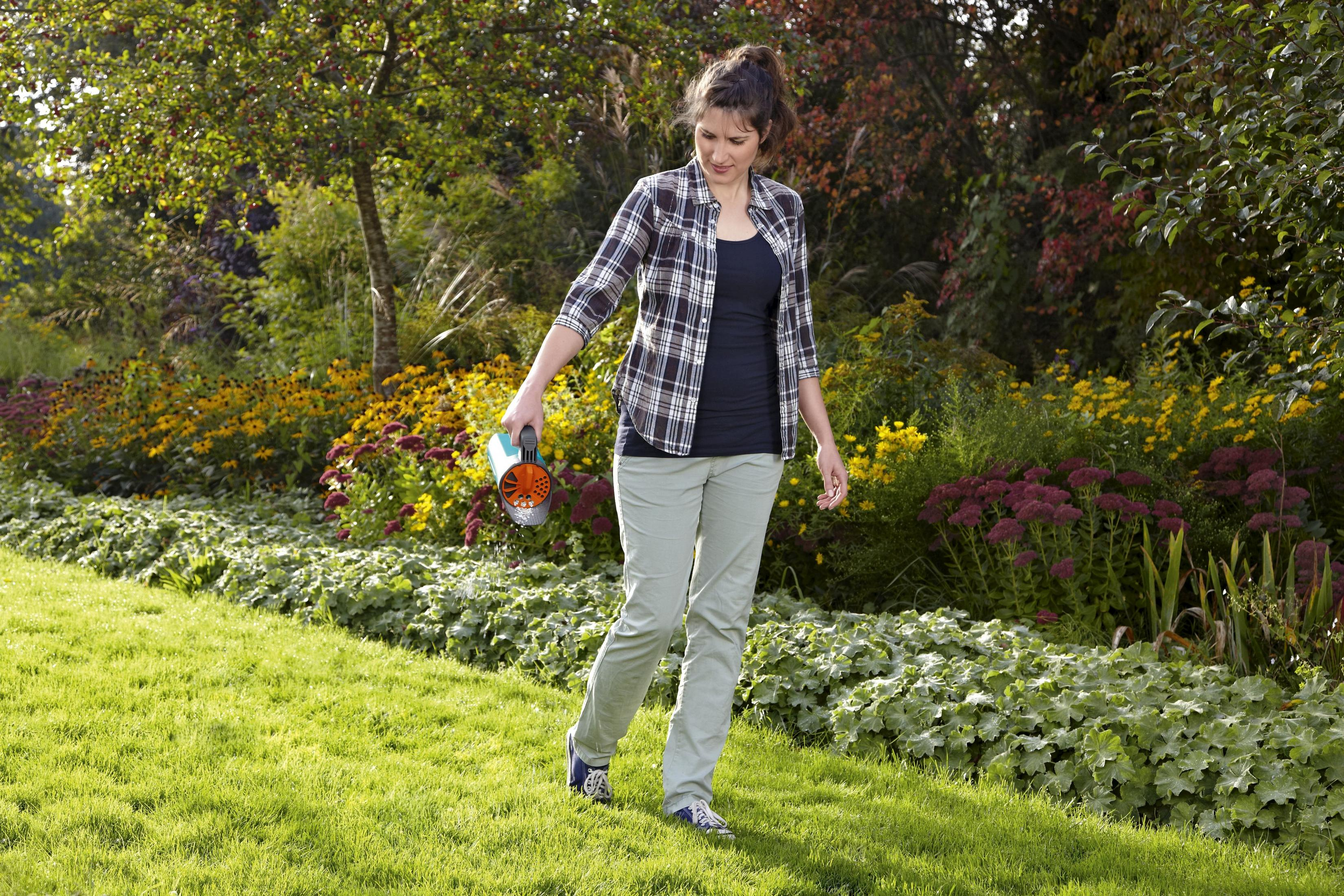 Kobieta podlewa rośliny w bujnym ogrodzie z żółtymi i czerwonymi kwiatami.