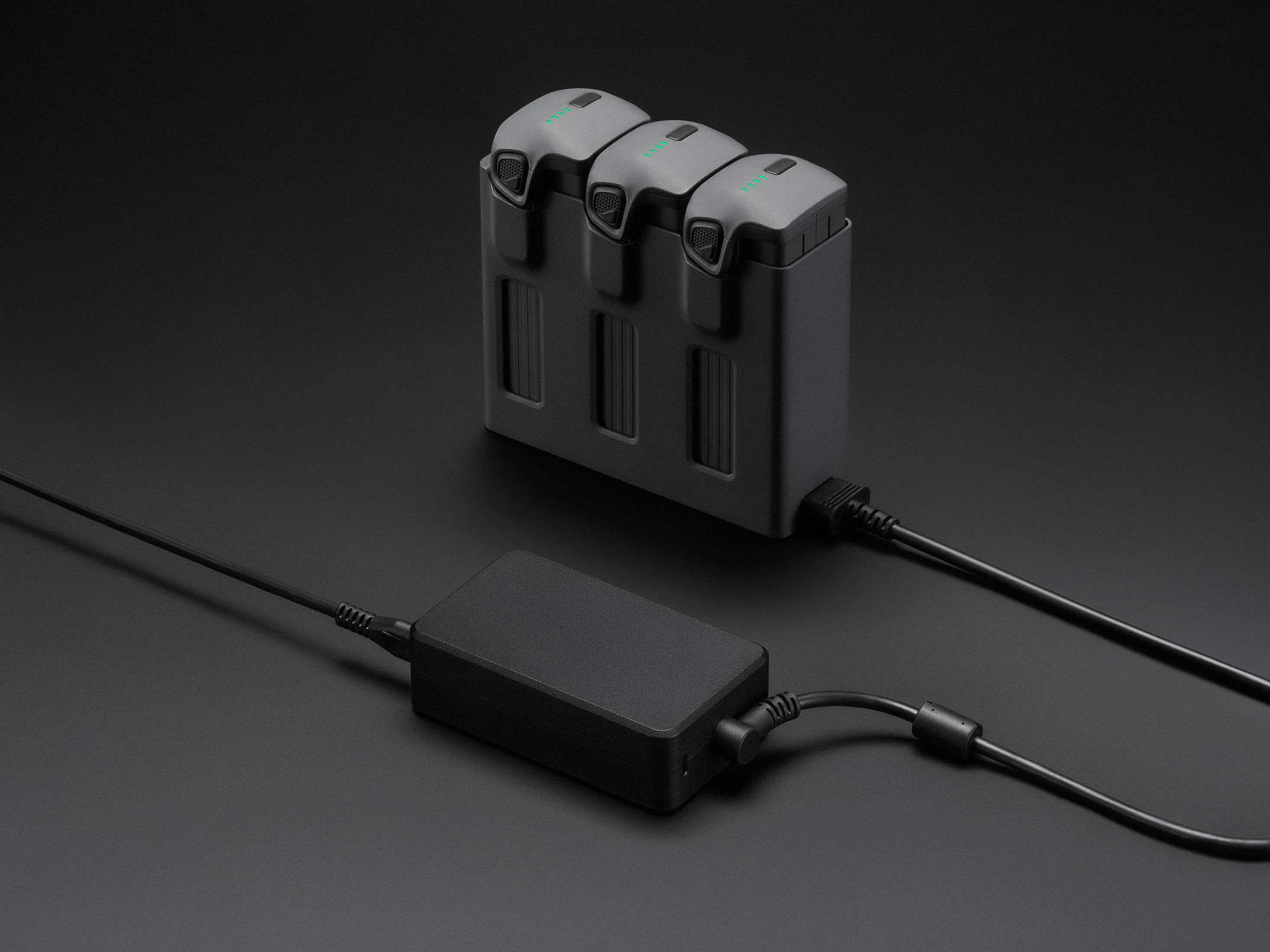 Tres baterías grises en un centro de carga con adaptador de corriente negro.