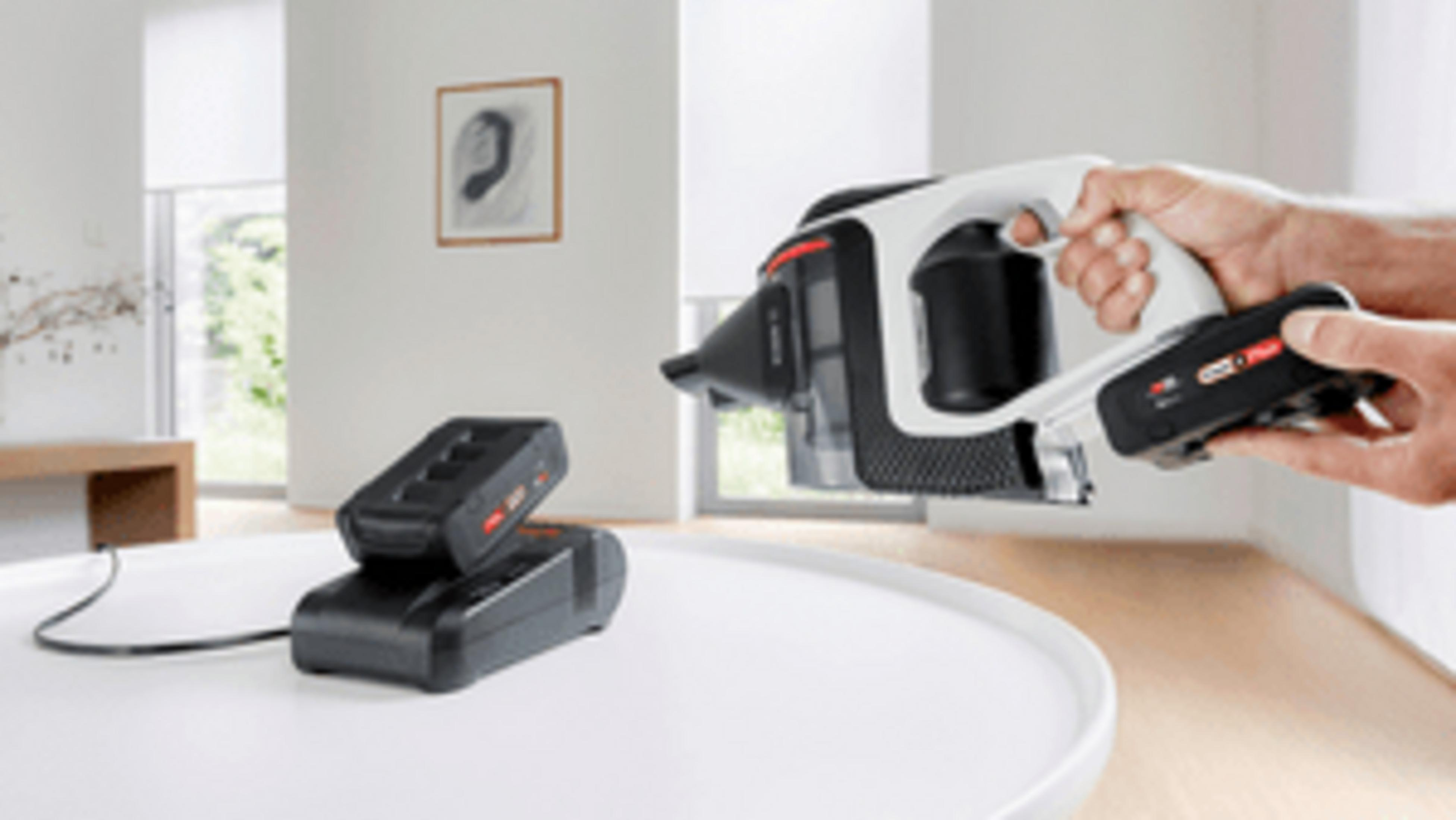 Ein Mann hält einen Akku-Staubsauger, daneben Ladegeräte auf einem Tisch.