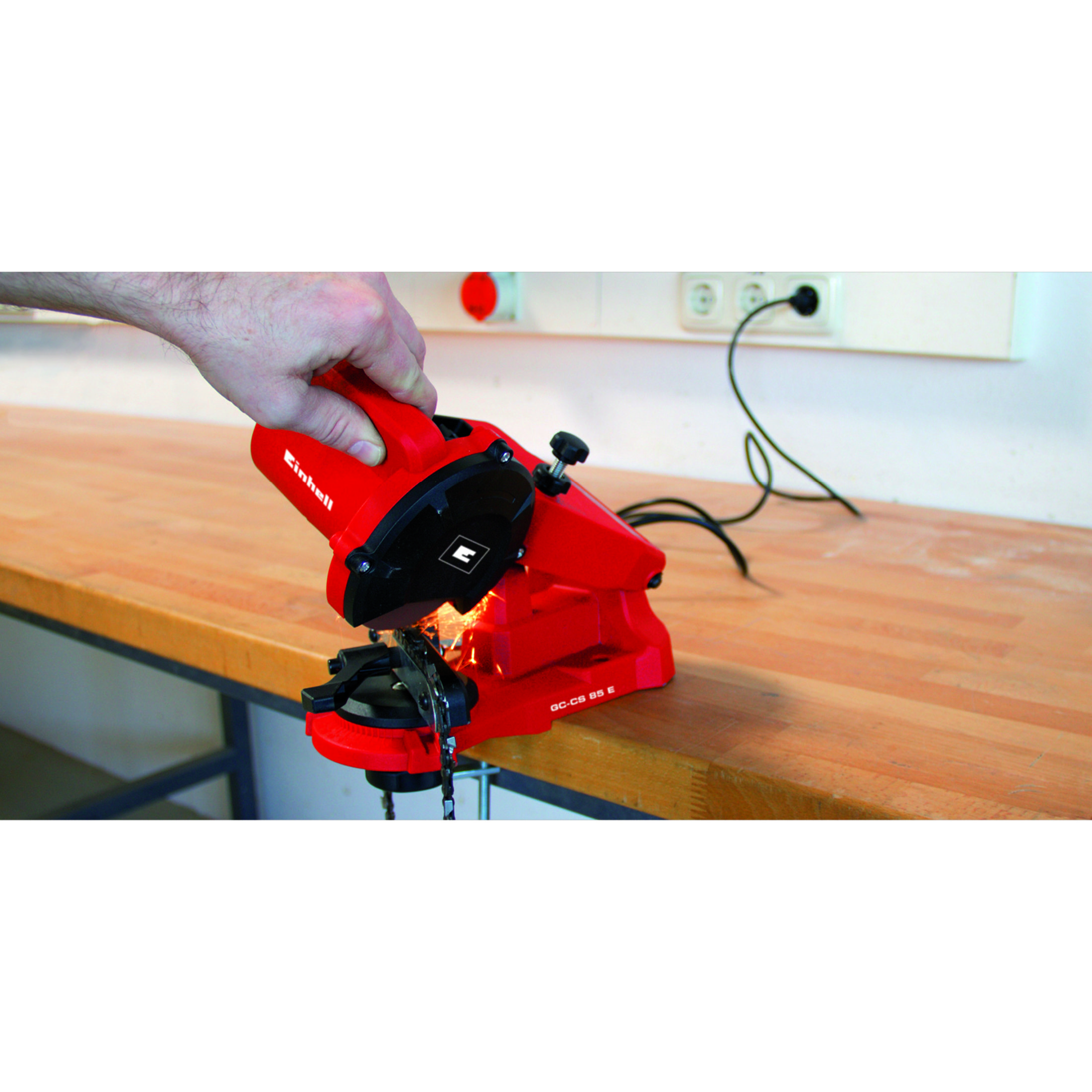 Eine rote Kettenschärfmaschine mit Funkenflug auf einem Holztisch.