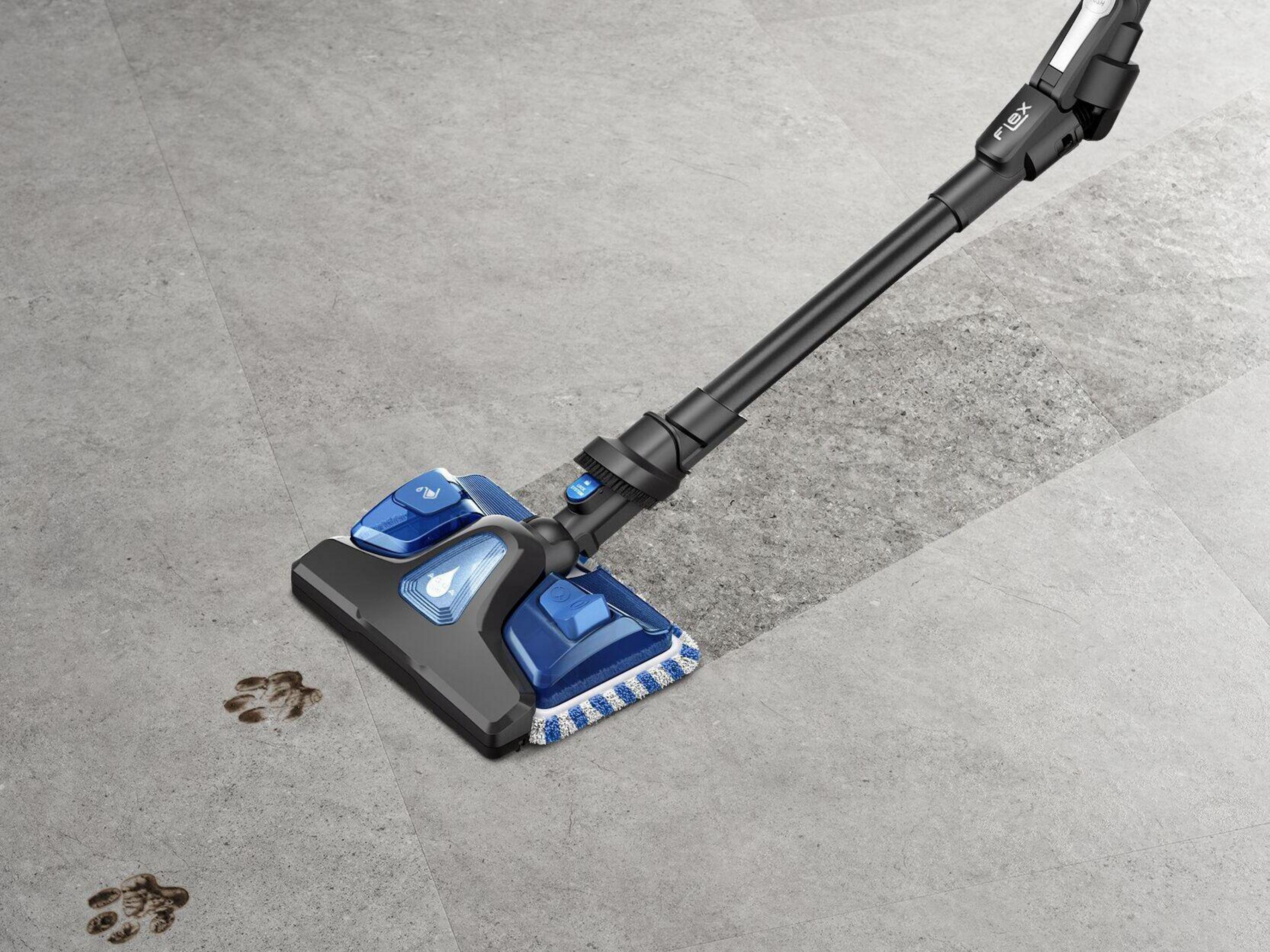 Un aspirapolvere bagnato/asciutto blu pulisce impronte di zampe su un pavimento piastrellato grigio.