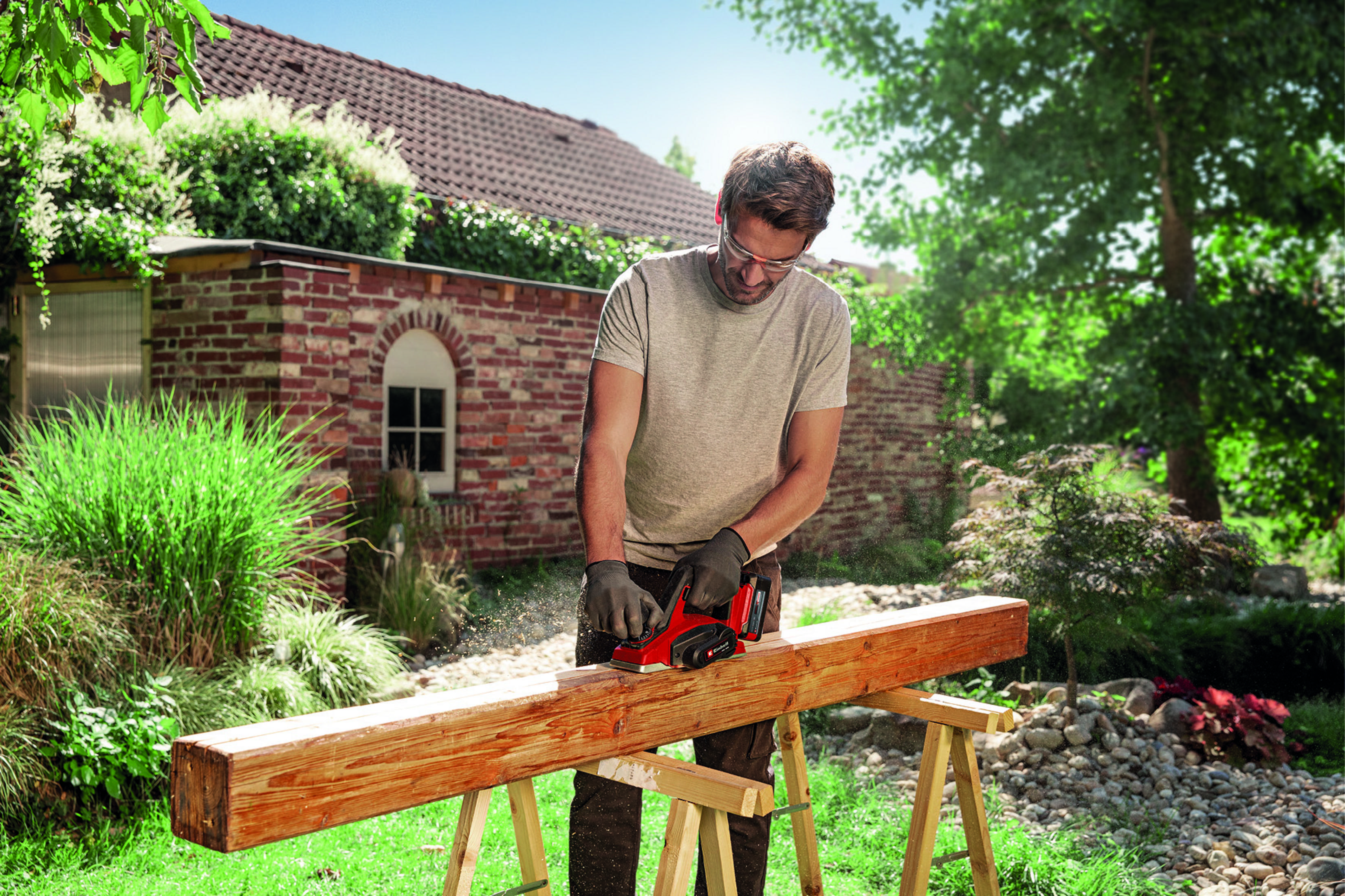 Mężczyzna struga drewno w ogrodzie. Lecą trociny.