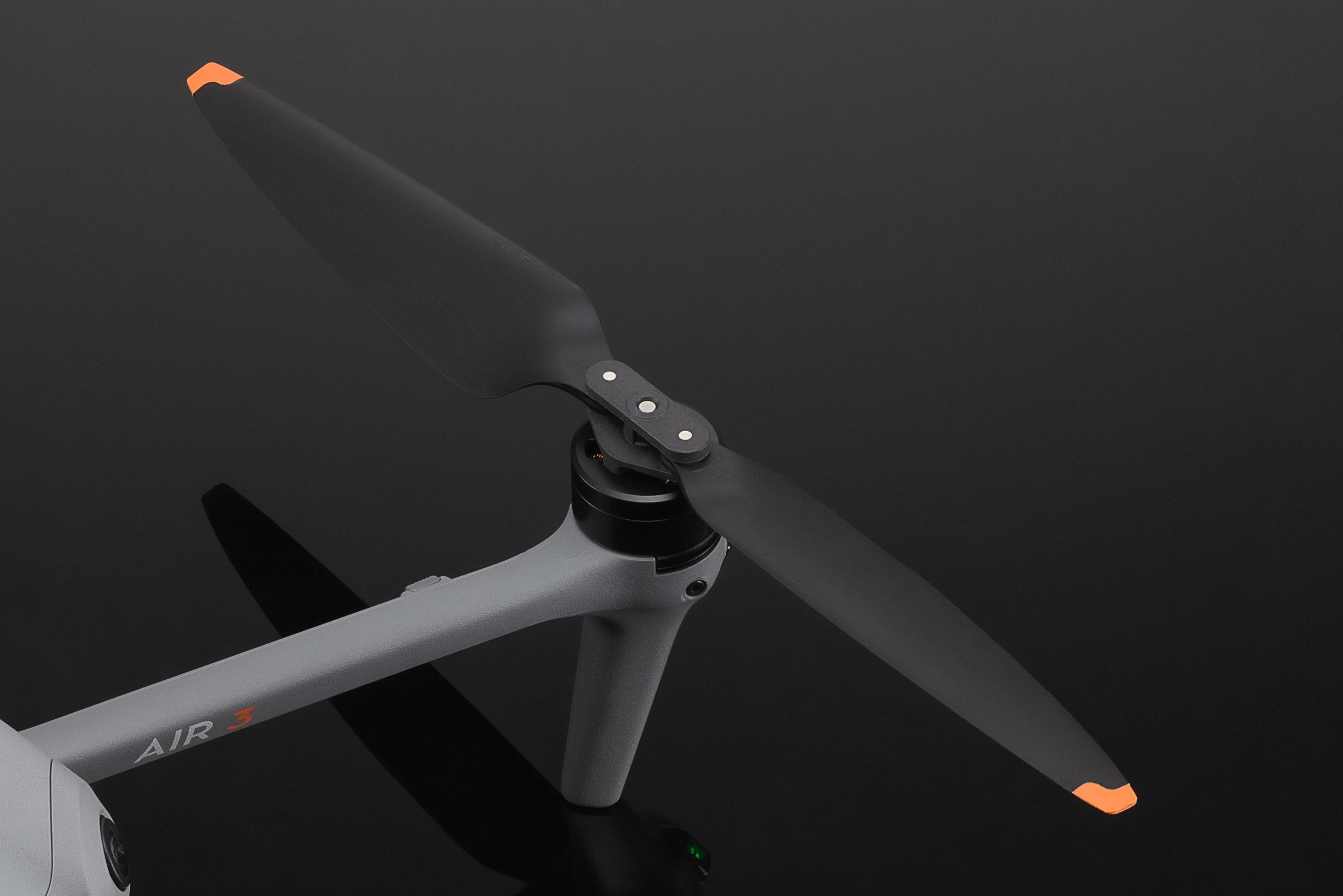 Grijze dronearm met zwarte propeller en oranje tips op donkere achtergrond.