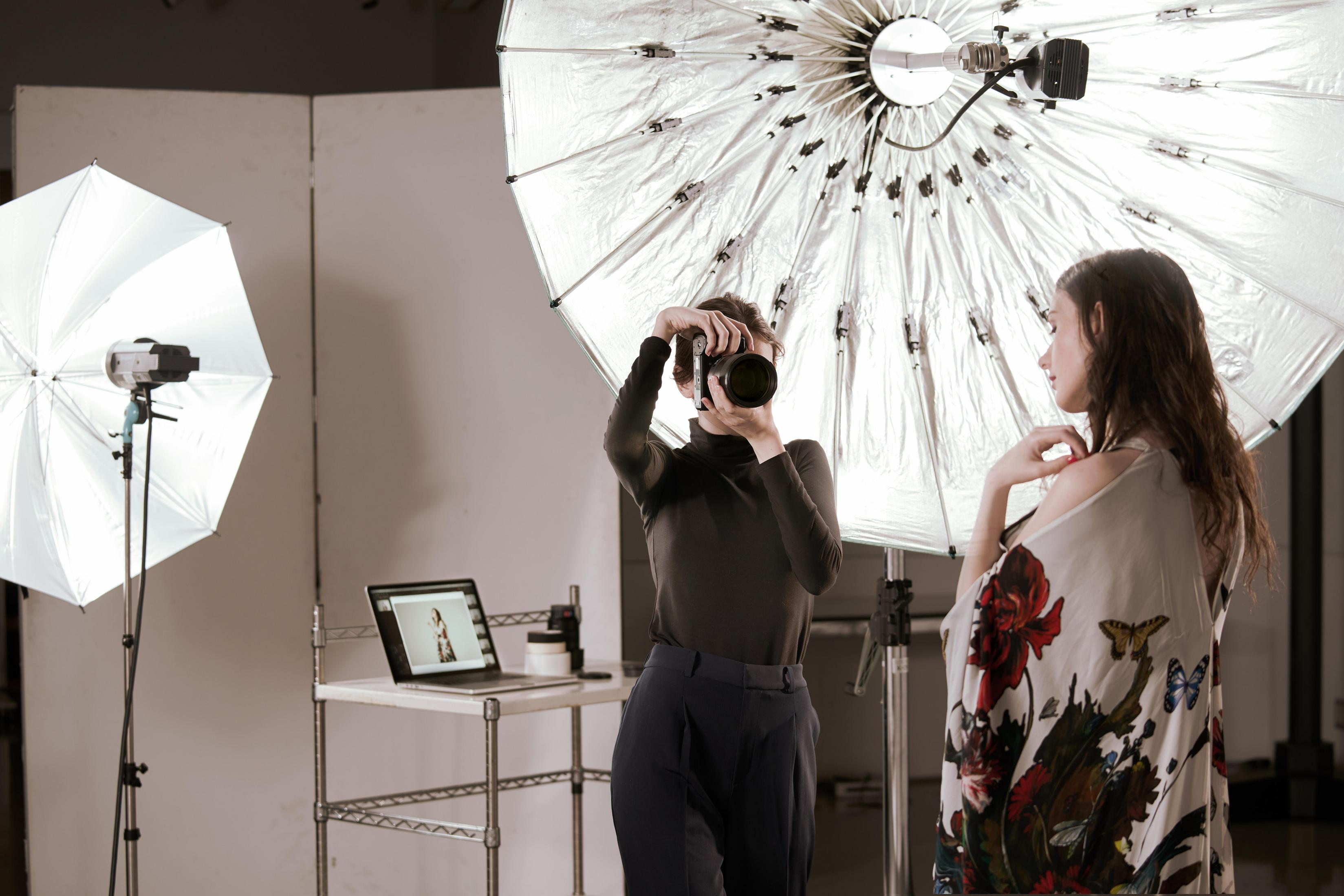 Photographer taking photo of model with large light umbrella, laptop nearby.