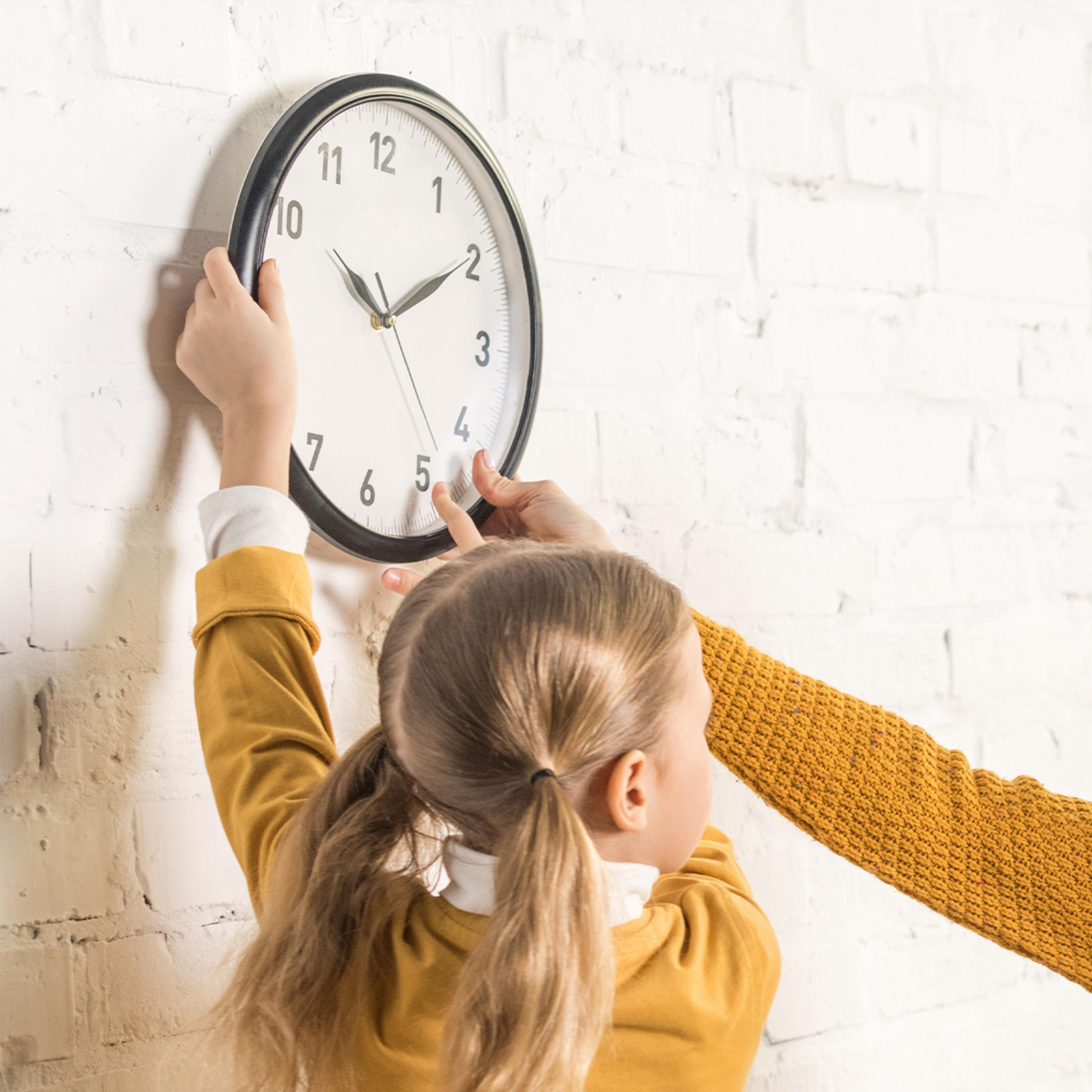 Ein Kind und eine erwachsene Person hängen eine Uhr an eine weiße Ziegelwand.