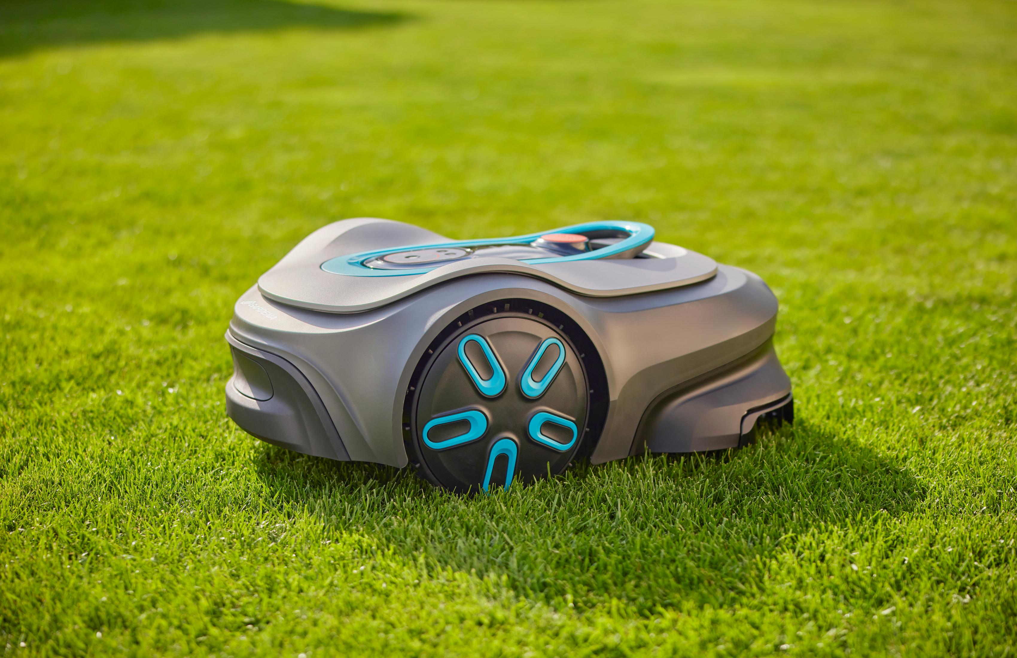 Szara kosiarka automatyczna z niebieskimi akcentami stoi na zielonym trawniku.