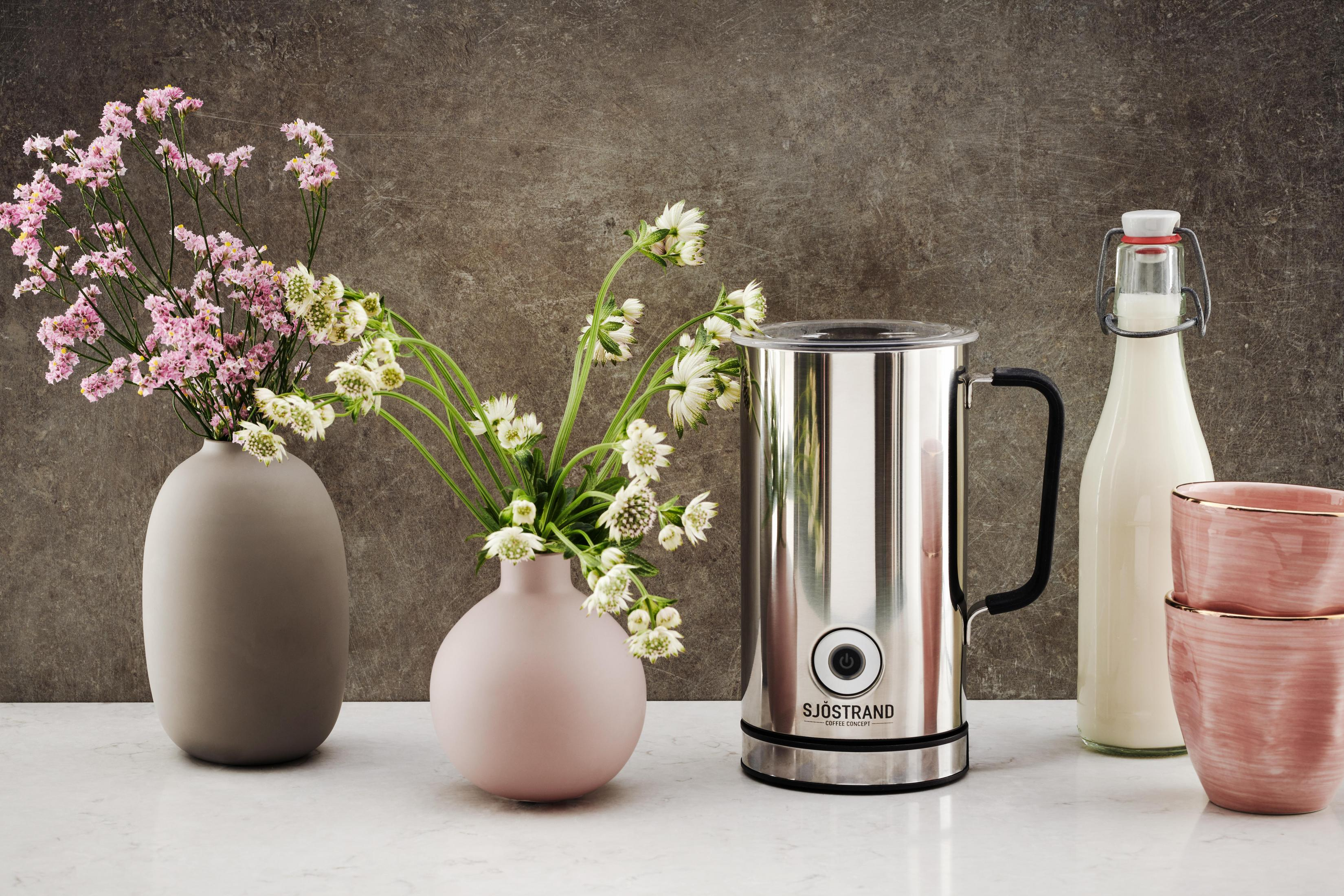 Zwei Vasen mit Blumen, Milchflasche, Metallkännchen und rosa Tassen.