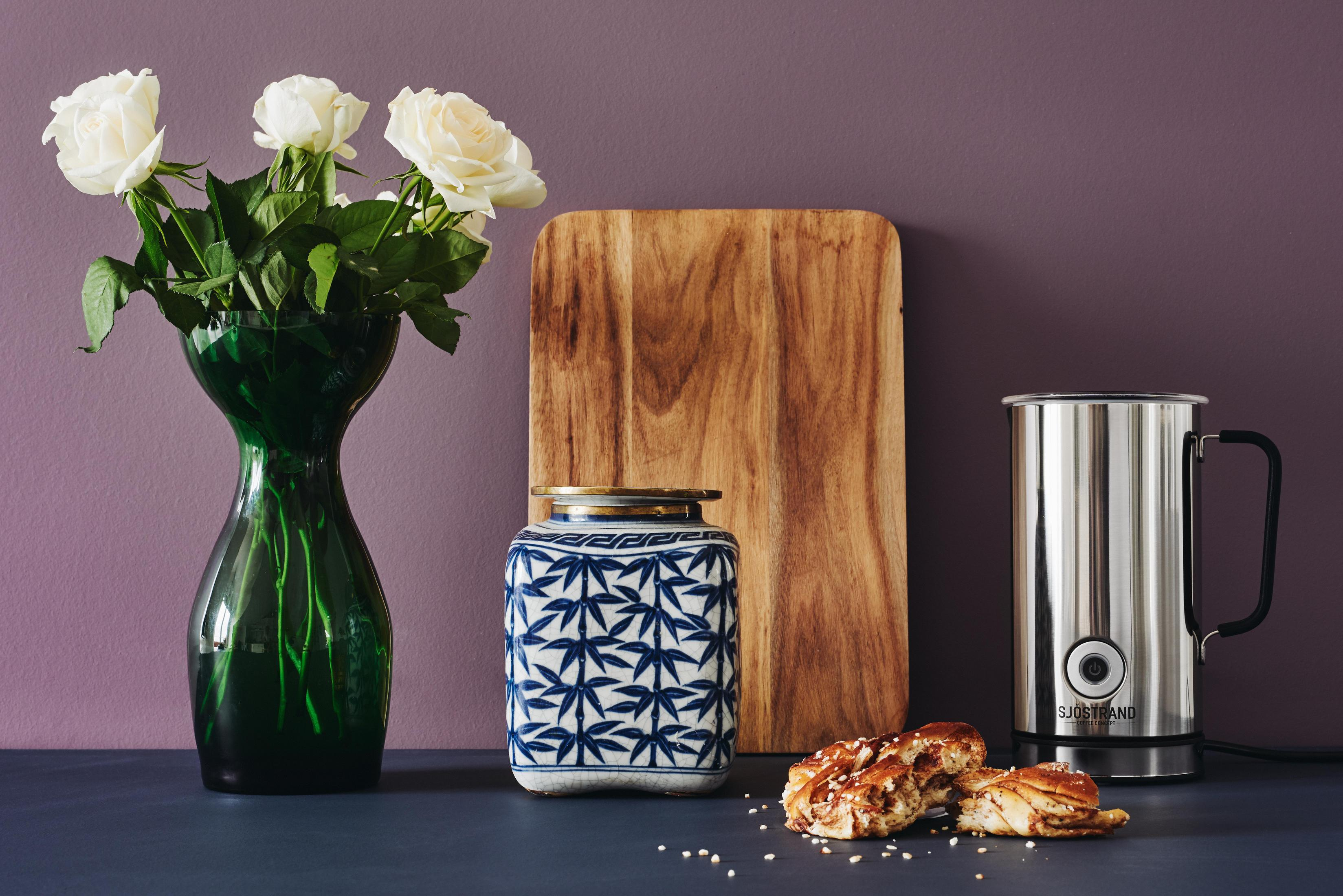 Weiße Rosen in einer grünen Vase, eine blaue Vase, ein Holzbrett und ein Milchaufschäumer.