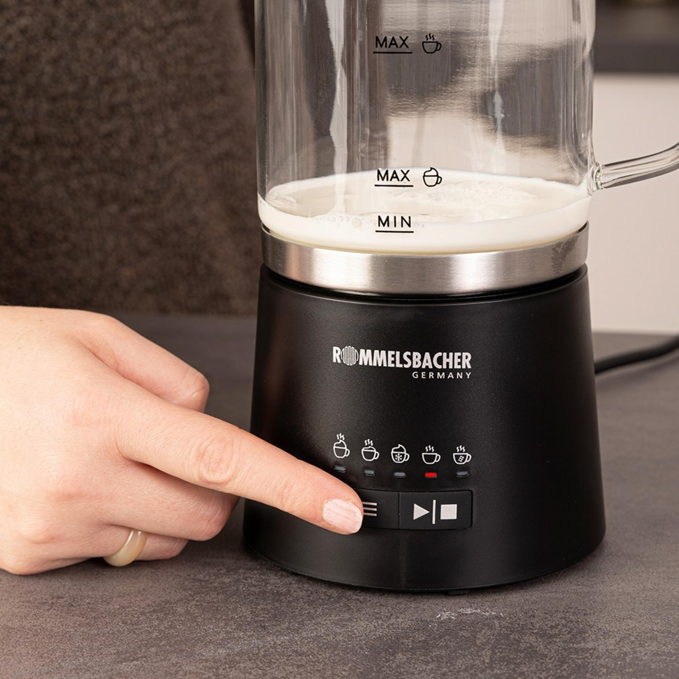 Eine Hand drückt auf die Tasten eines schwarzen Milchaufschäumers mit Glasbehälter.