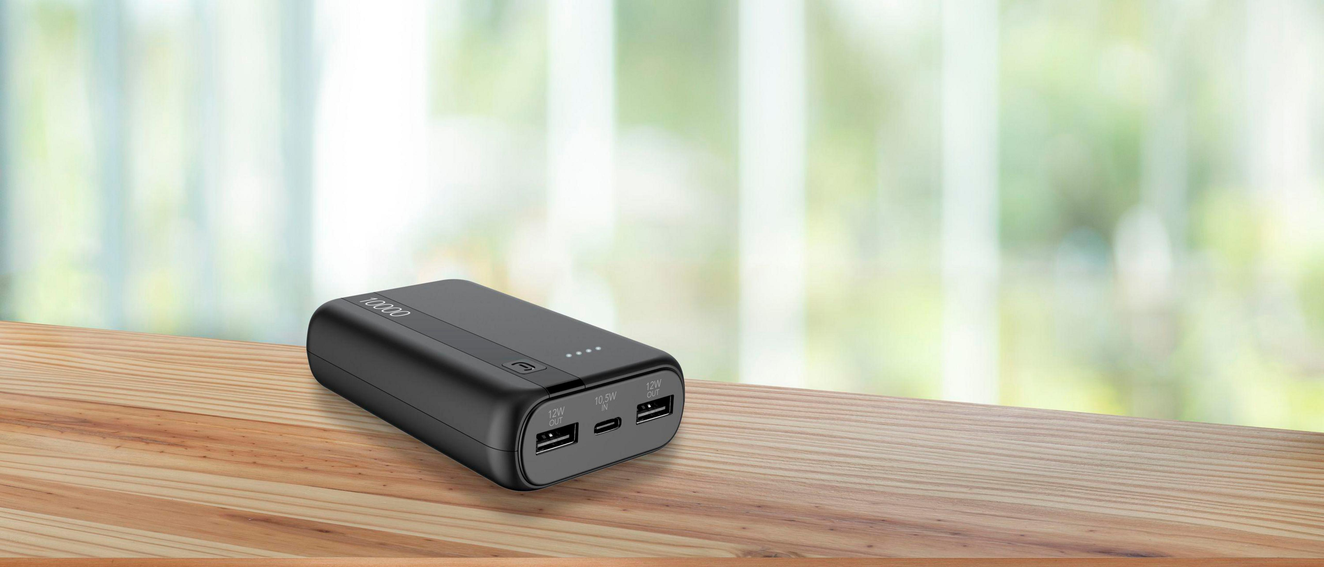 Schwarzes Powerbank mit 10000 Kapazität auf Holztisch, unscharfer Hintergrund.