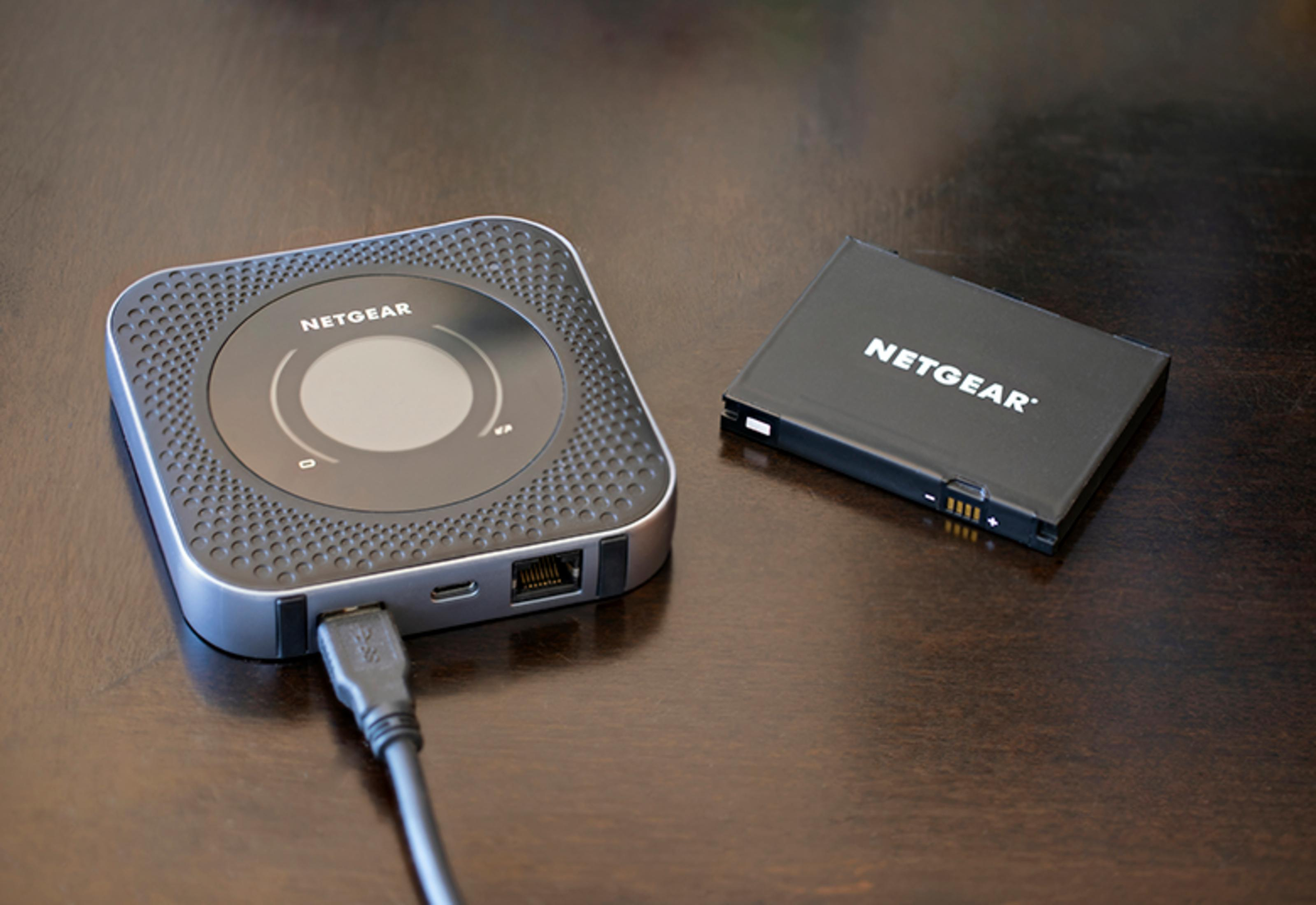 Router Netgear z kablem USB i bateria Netgear na drewnianym stole.