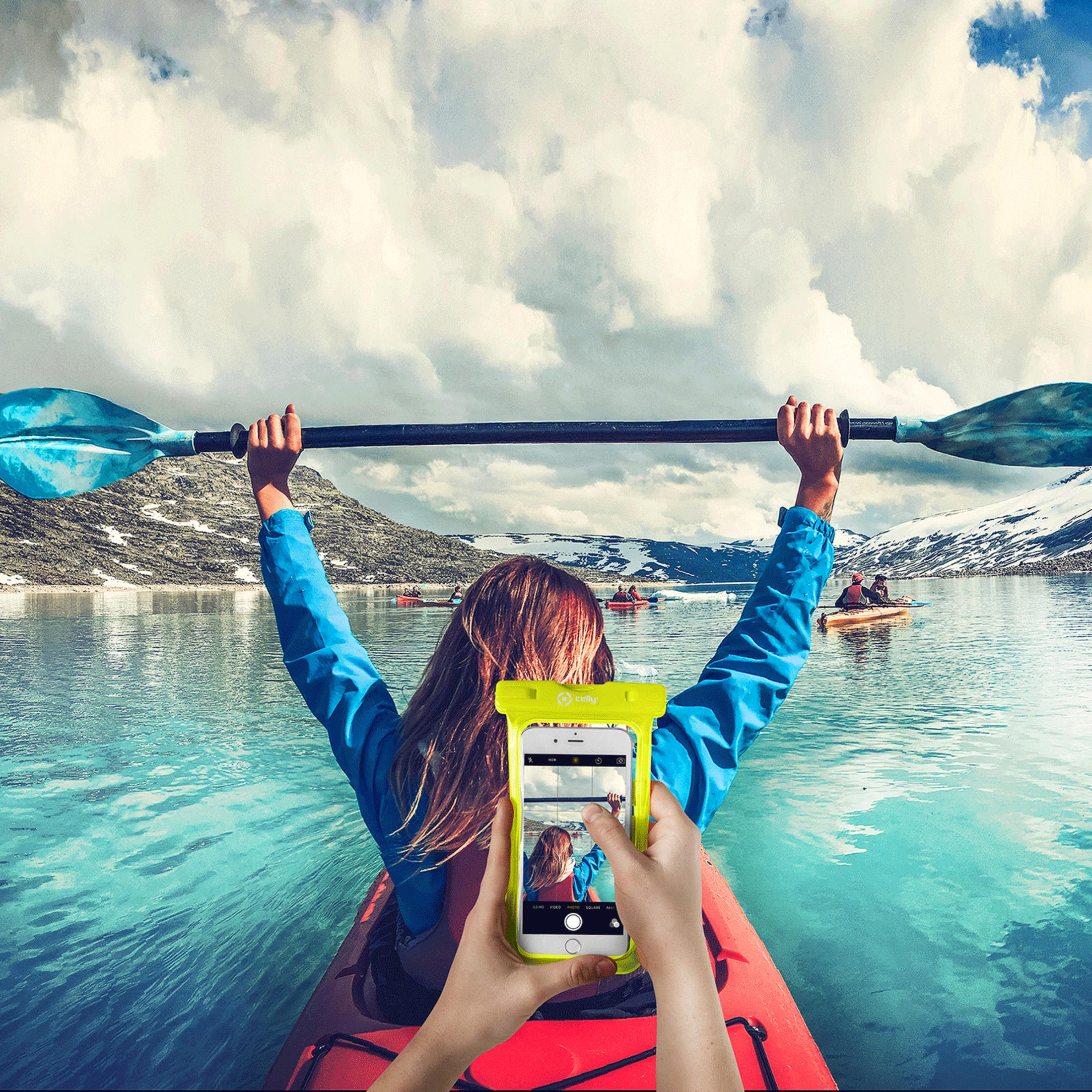 Person im Kajak hält Paddel, macht Foto von sich mit Handy vor schneebedeckten Bergen.