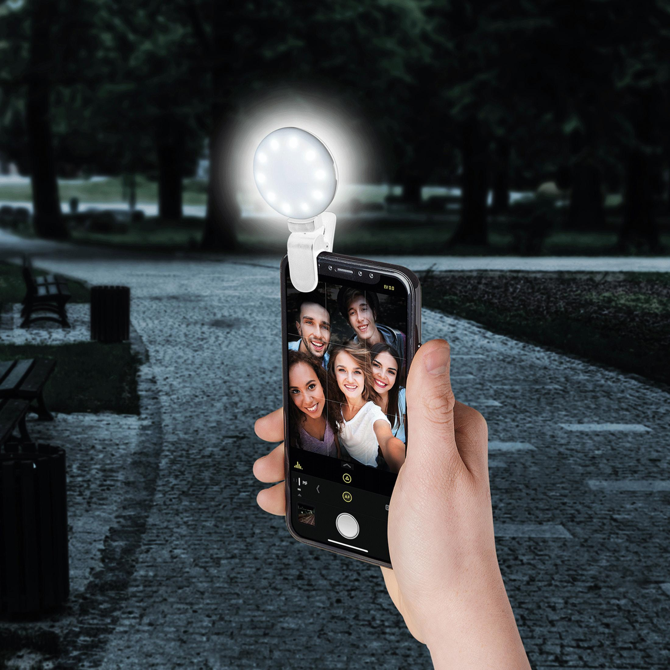 Mano sostiene teléfono con luz selfie, mostrando cinco caras sonrientes en parque.