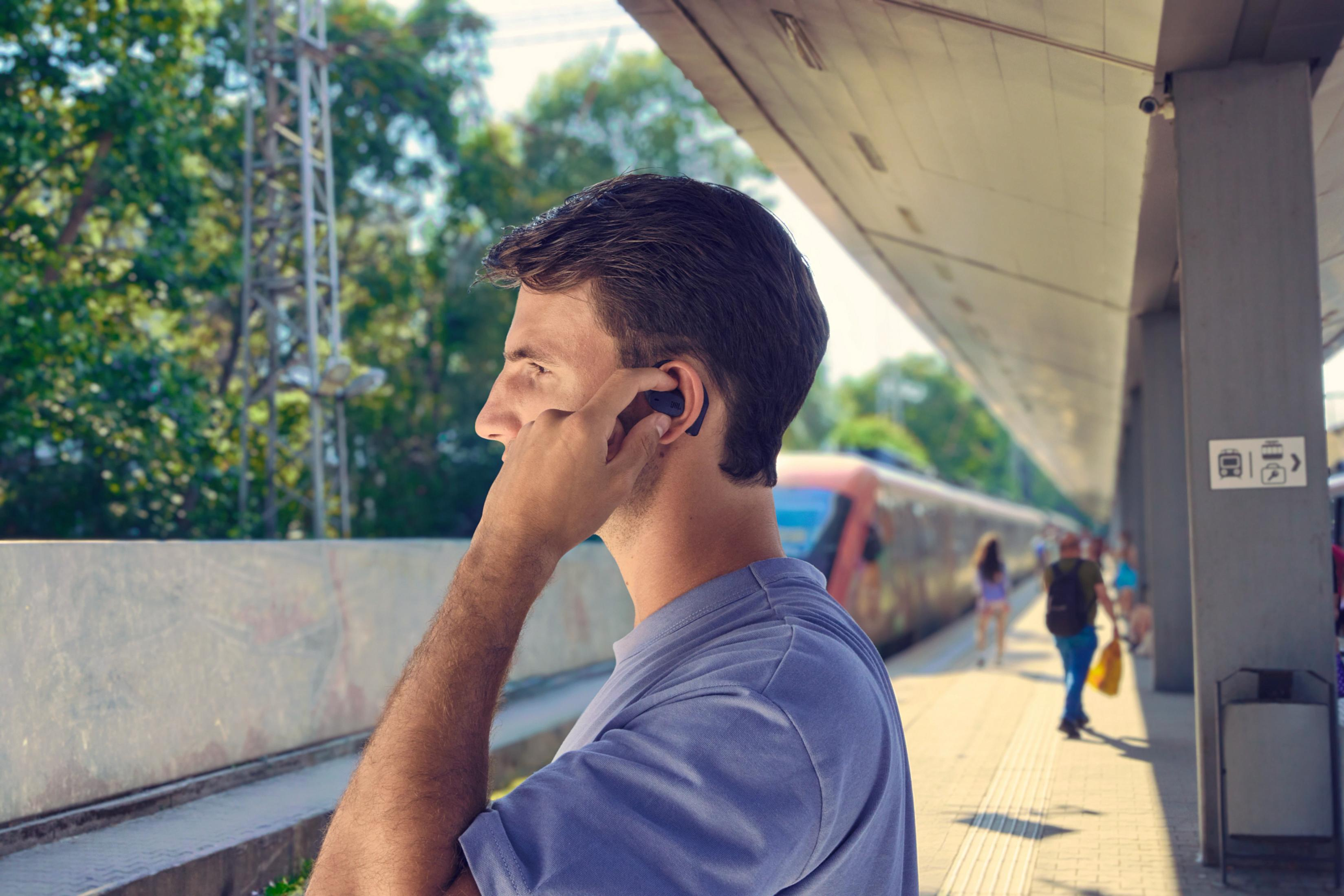 Uomo sulla banchina con auricolari, treno sullo sfondo.