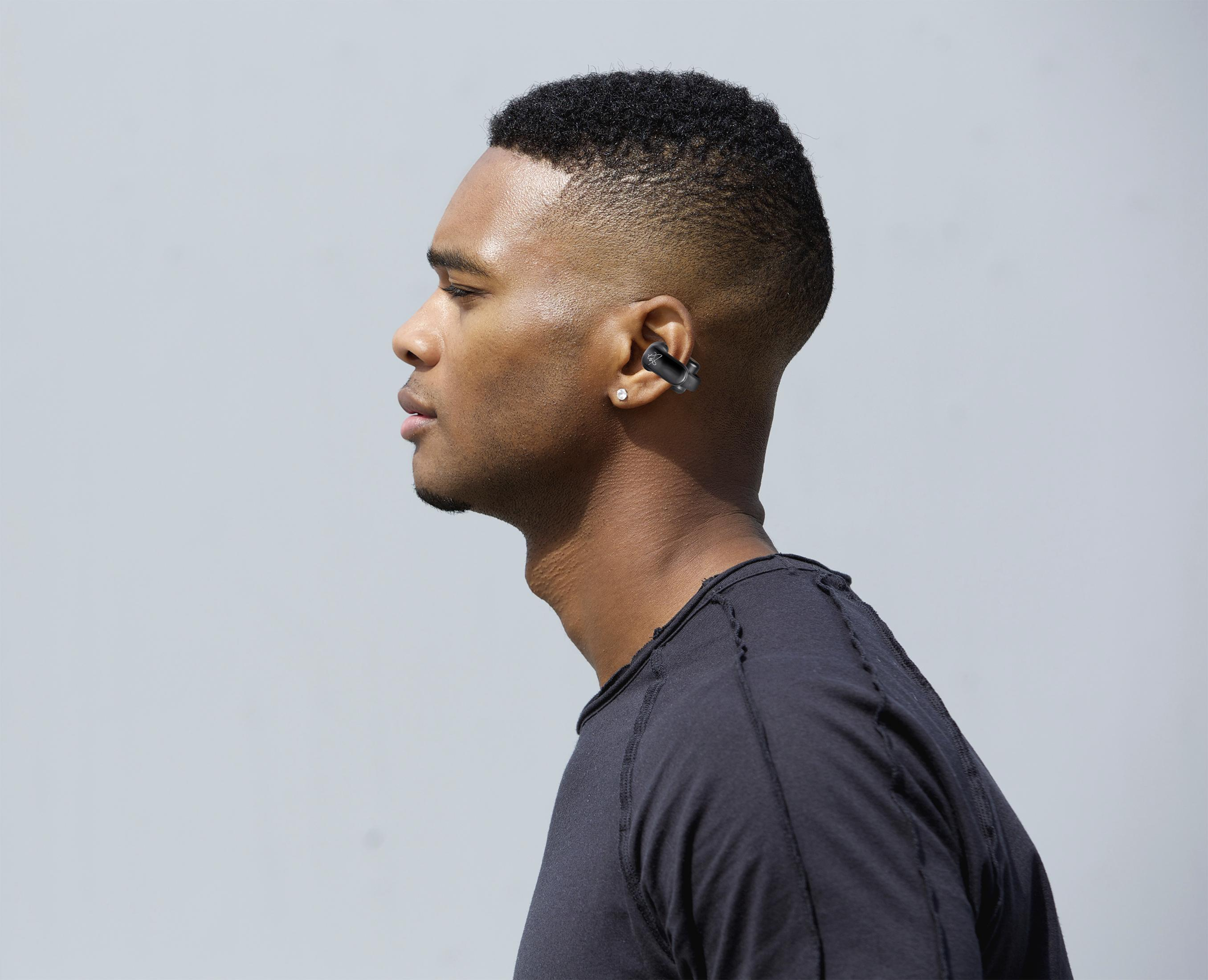 Un hombre con pelo corto y negro lleva una camiseta negra y un auricular negro.