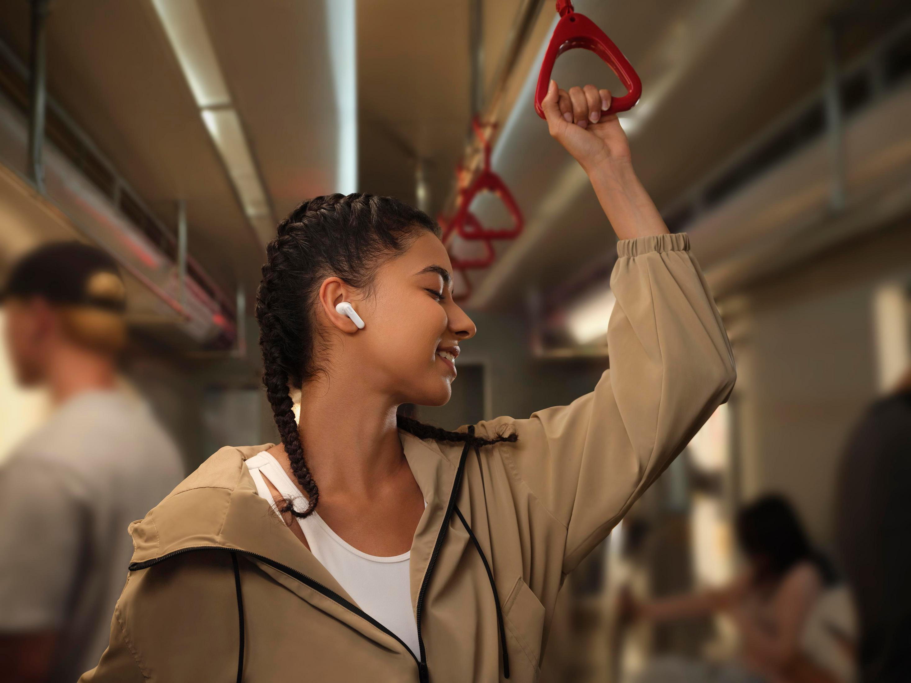 Femme avec des écouteurs dans un train, tenant une poignée rouge.