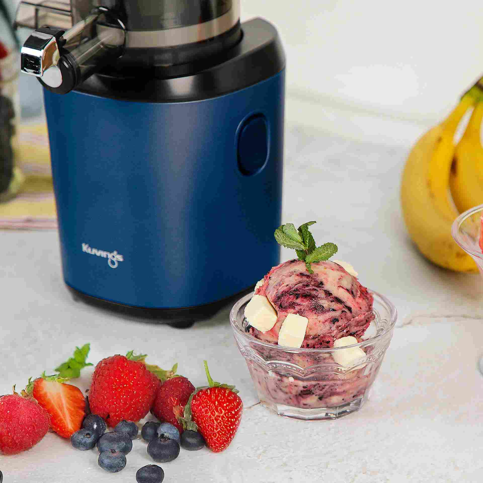 Centrifuga blu accanto a bacche, gelato e banane su tavolo bianco.