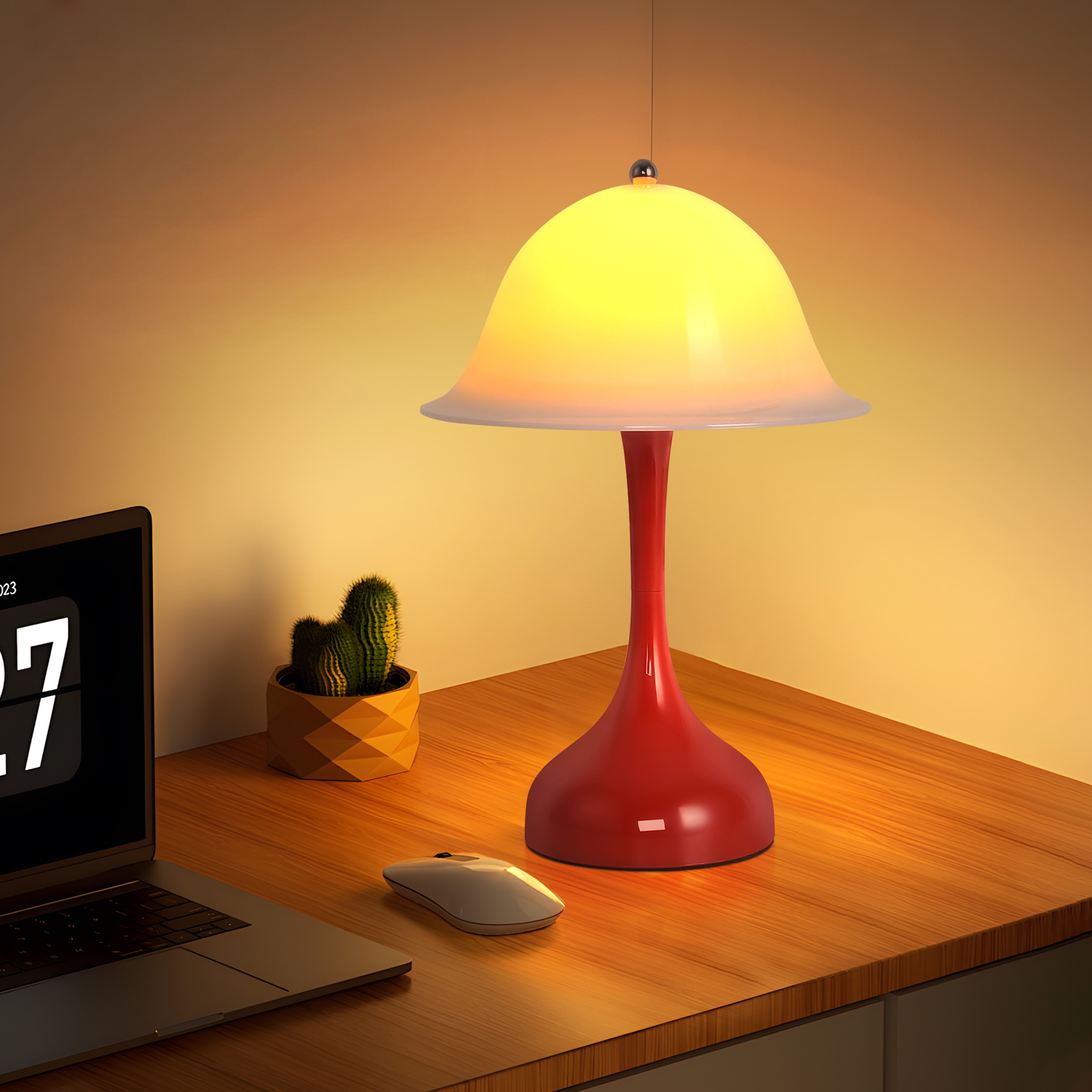 Base rossa di una lampada da scrivania con paralume giallo, accanto a un laptop e un cactus.