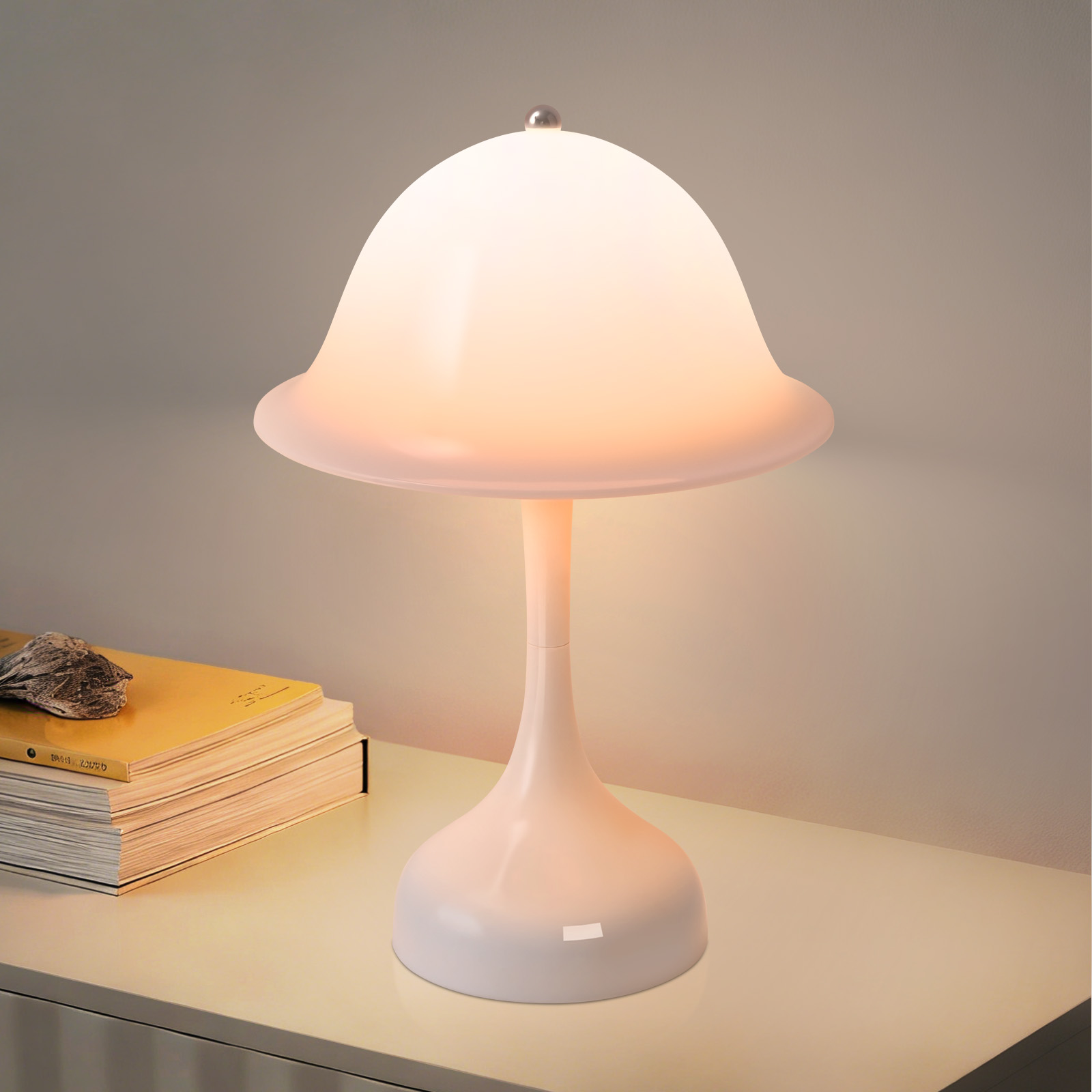 Una lampada bianca a fungo è su un tavolo accanto a una pila di libri gialli.
