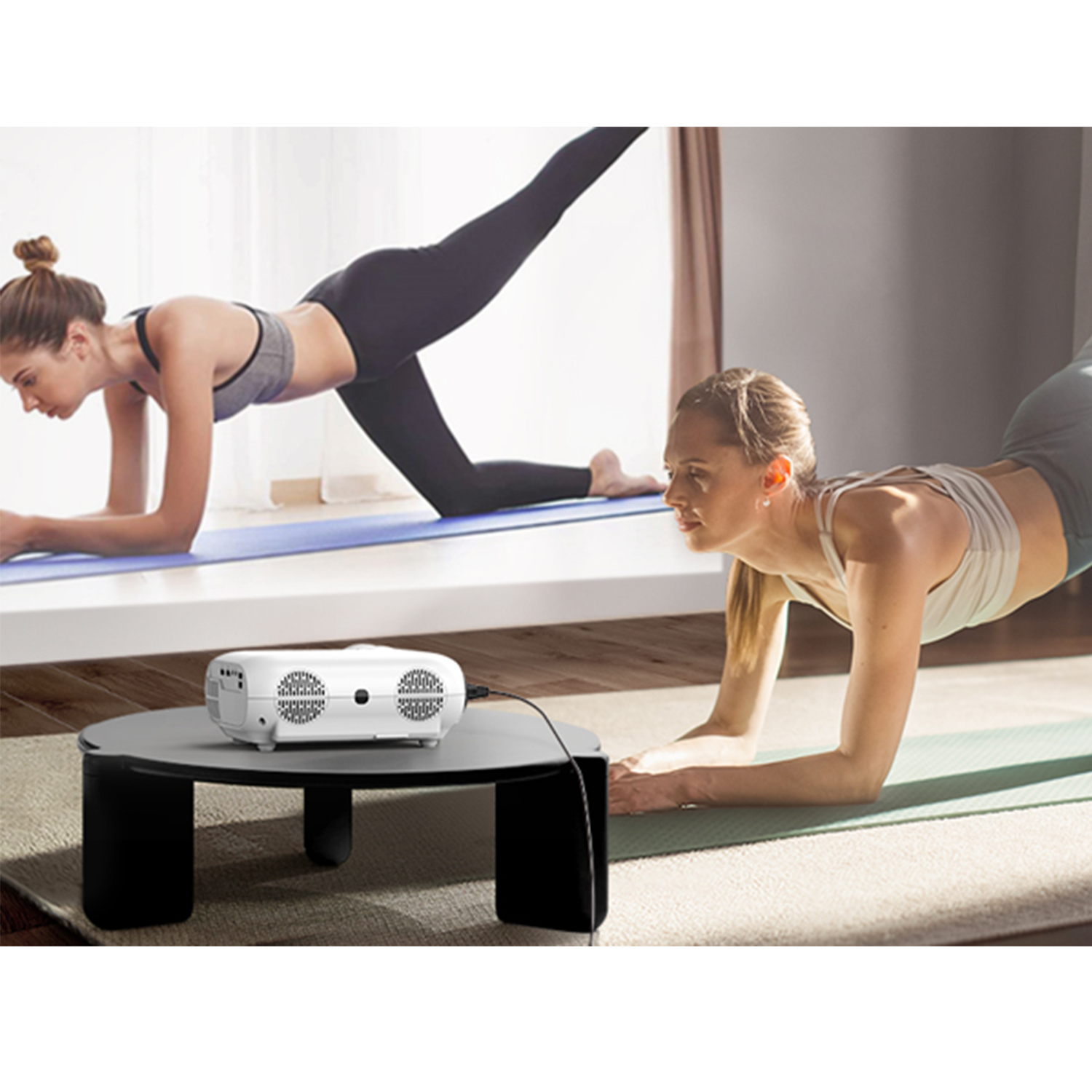 Zwei Frauen machen Yoga vor einem Projektor, der ein Bild auf eine Leinwand projiziert.