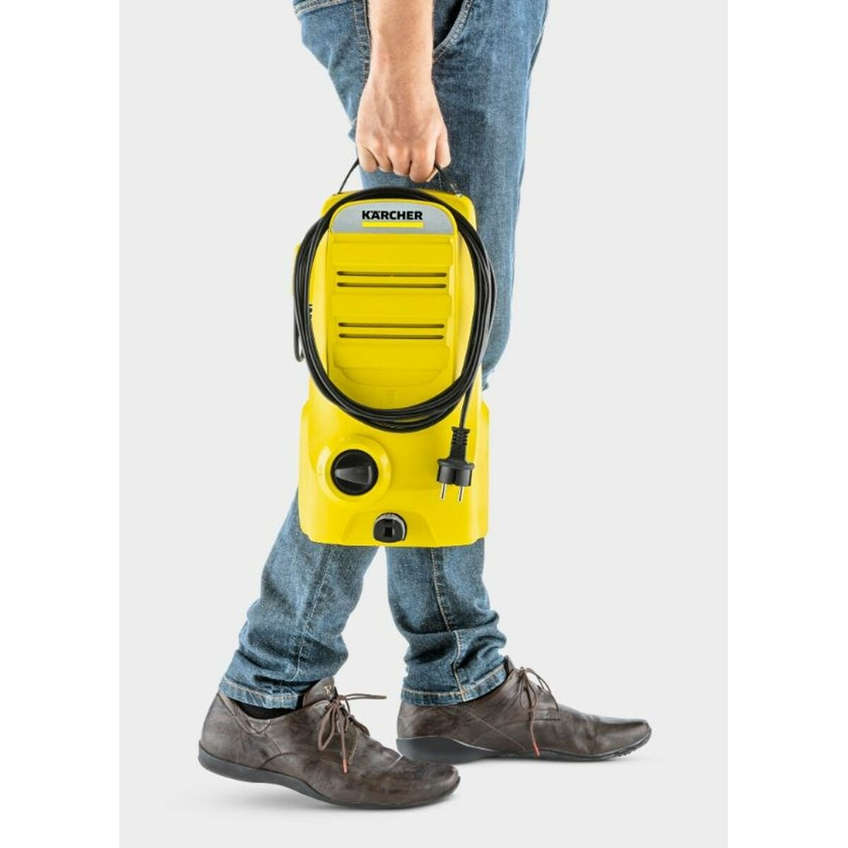 Osoba niosąca żółtą myjkę ciśnieniową Karcher z czarnym kablem.