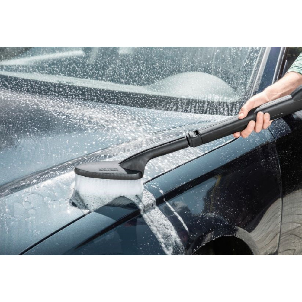 Ręka używa szczotki do mycia ciemnego samochodu z pianą.