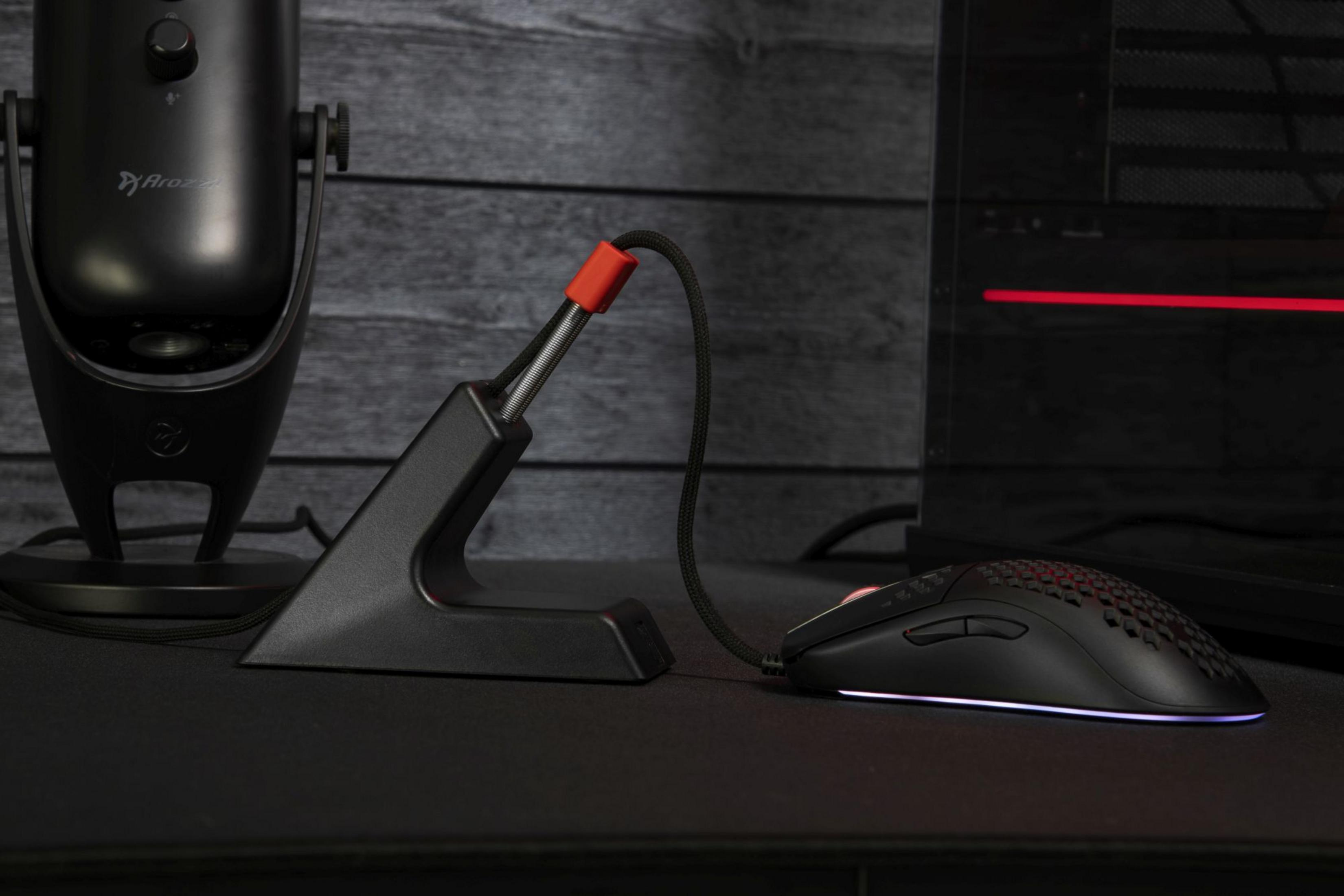 Mouse da gaming nero con illuminazione RGB accanto a un supporto microfono e PC.