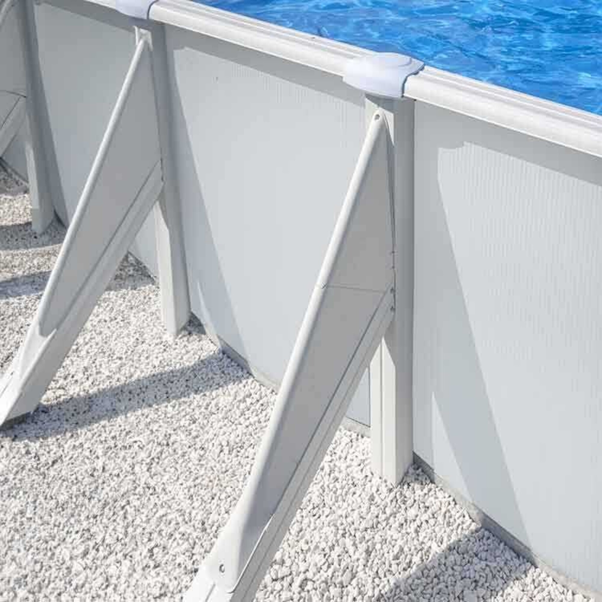 Una piscina elevada con pared blanca, agua azul y base de grava.