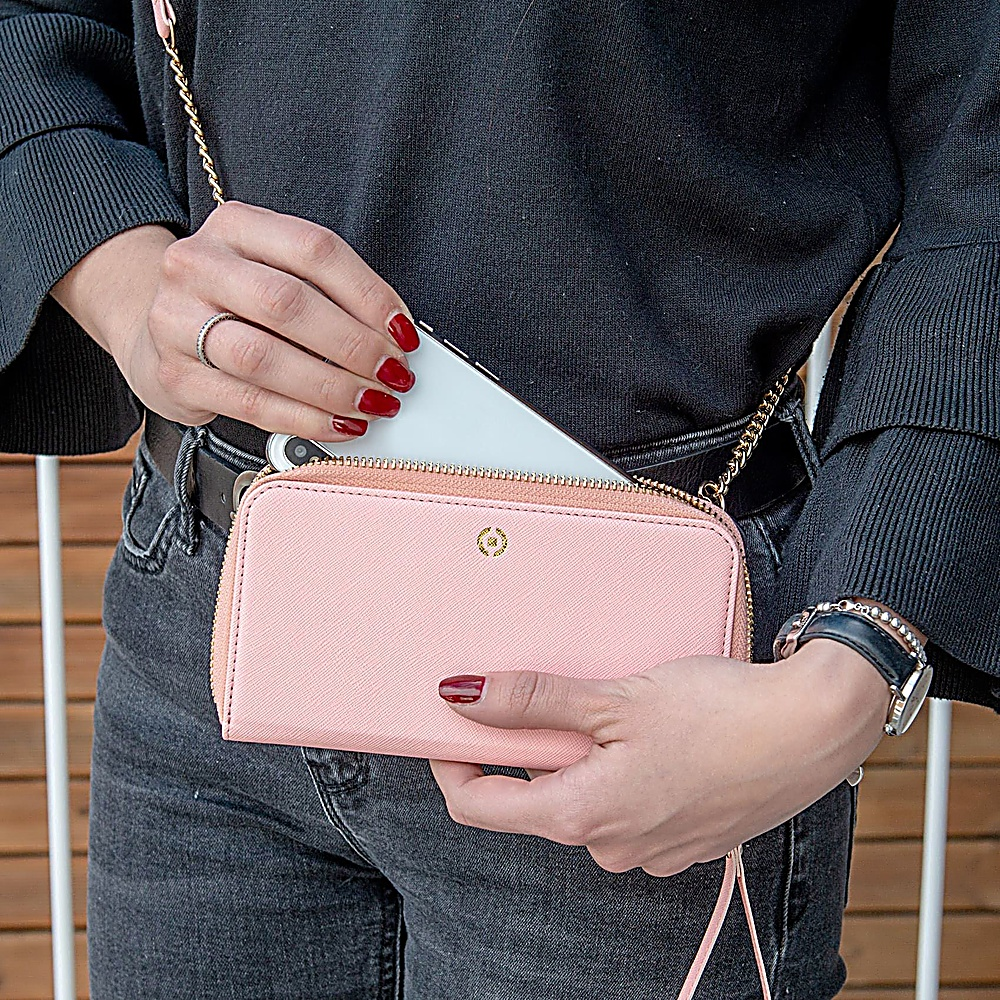 Una donna con le unghie rosse mette un telefono chiaro in un portafoglio rosa.