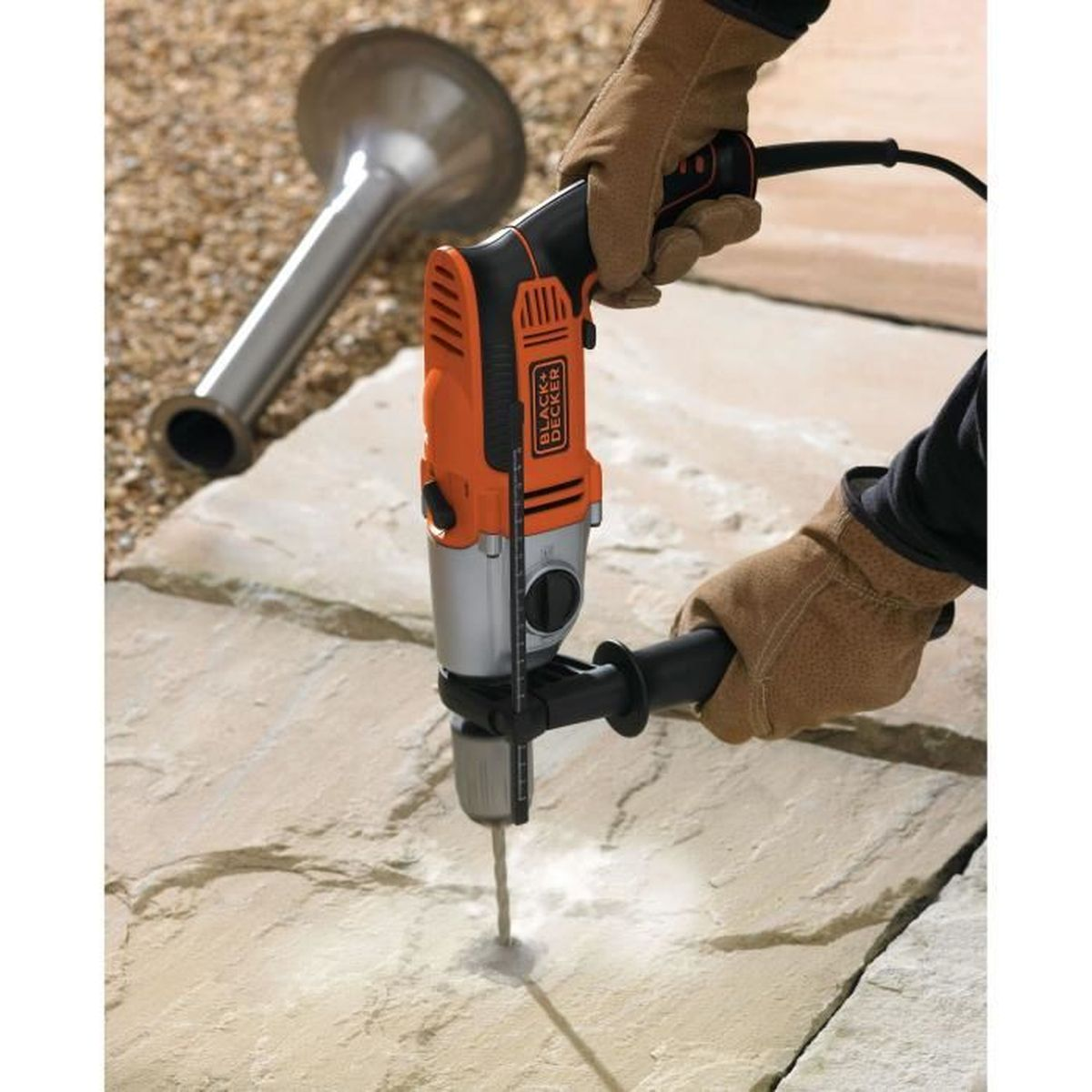 Ręka w rękawicy wierci w kamieniu pomarańczową wiertarką.