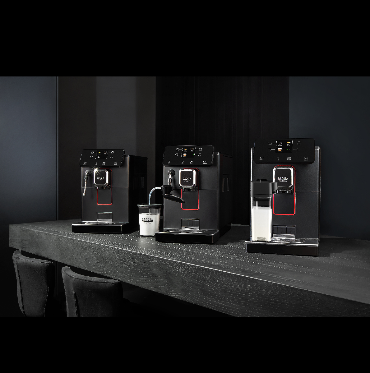 Drie zwarte koffiemachines met rode accenten op een donkerhouten aanrecht.