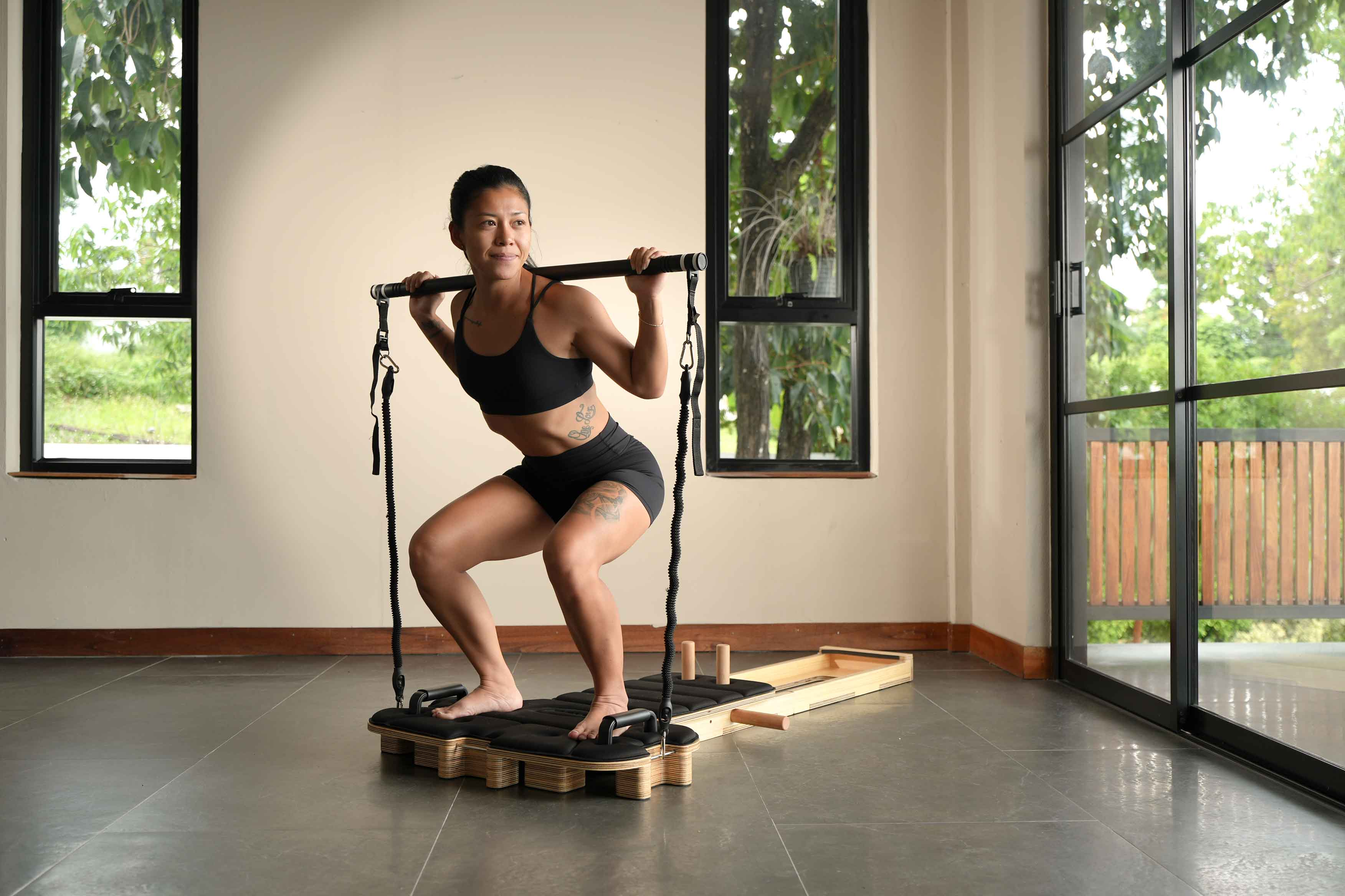 Kobieta robi przysiady z gumami oporowymi i drążkiem na urządzeniu fitness.