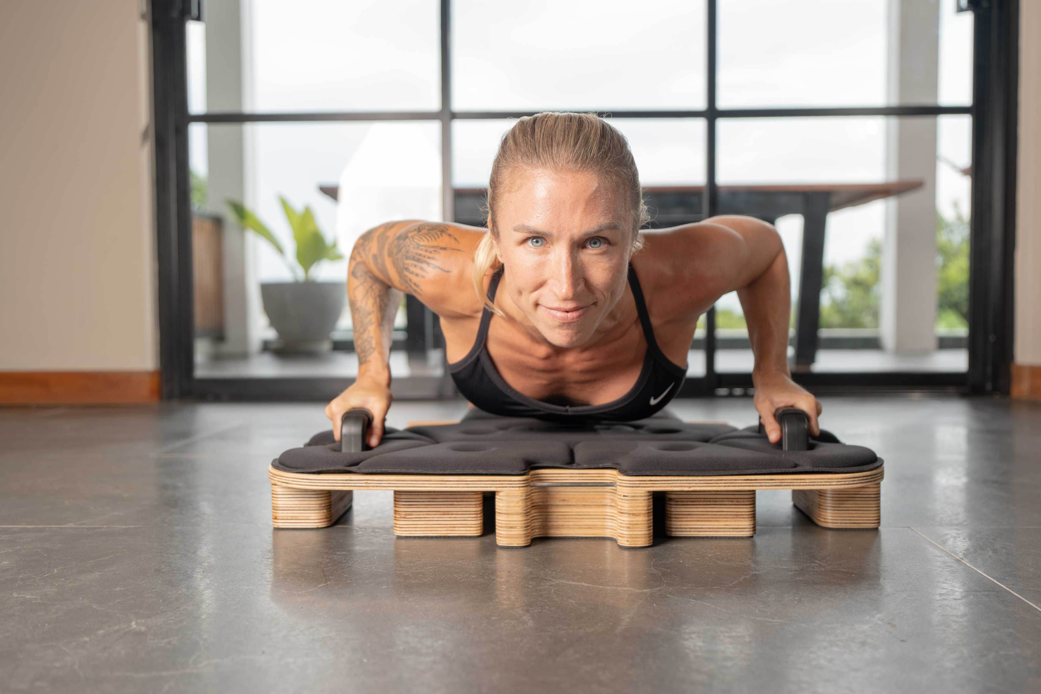 Kobieta wykonuje pompki na drewnianym stojaku z poduszką.