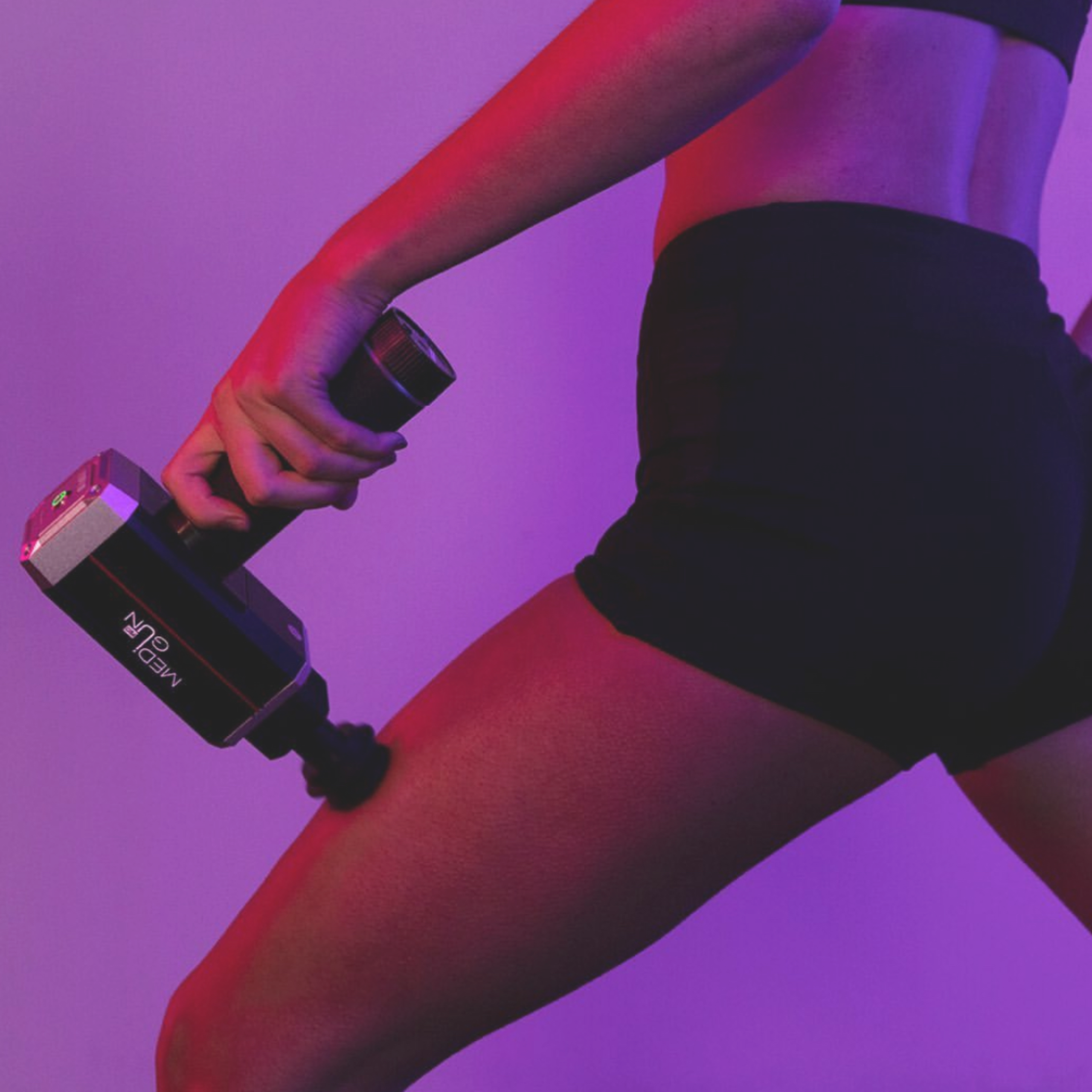 Dłoń trzyma pistolet do masażu na udzie osoby, w fioletowym świetle.