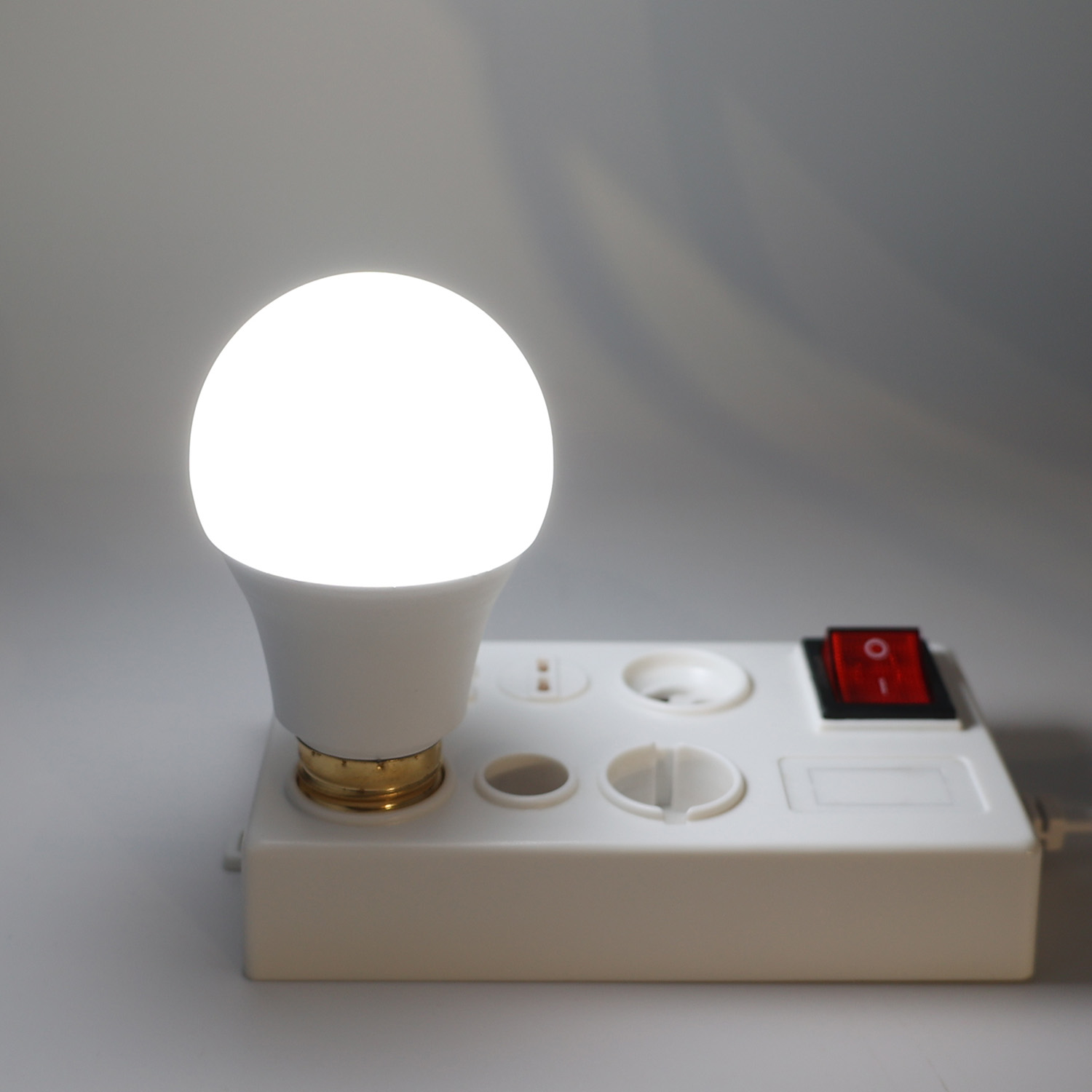 Una bombilla encendida está sobre una regleta blanca con un interruptor rojo.
