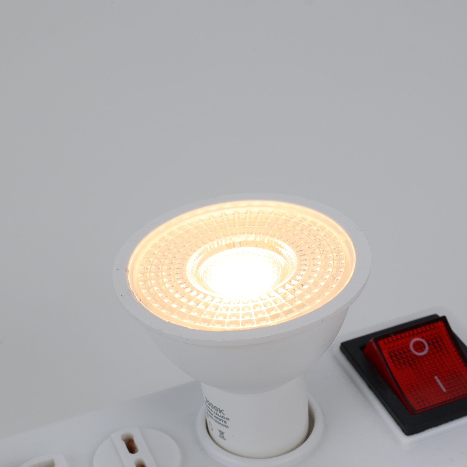 Una bombilla LED blanca se ilumina junto a un interruptor rojo en una regleta blanca.