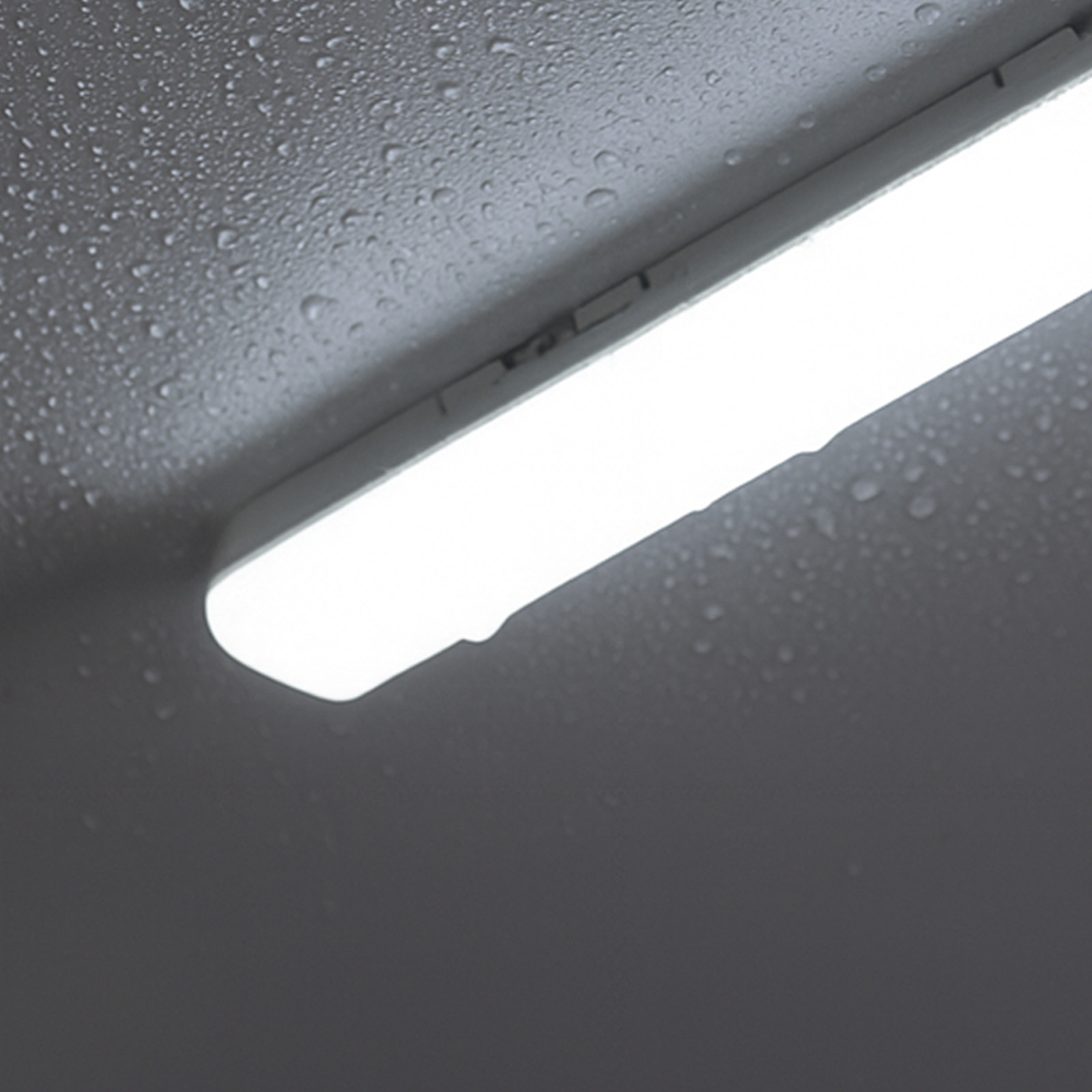 Una lámpara fluorescente blanca con gotas de agua sobre un fondo oscuro y texturizado.
