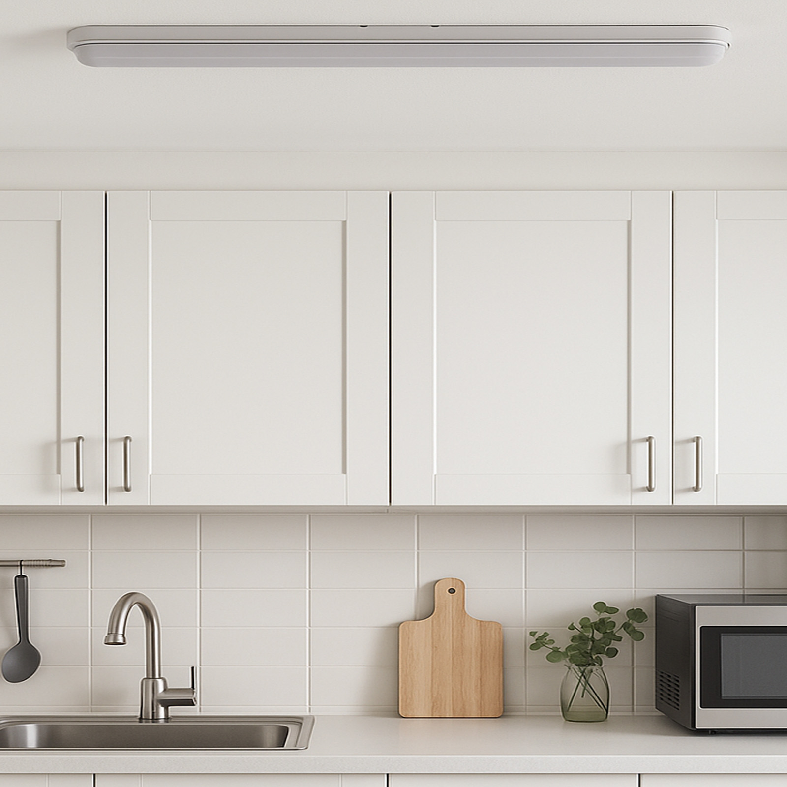 Armarios de cocina blancos sobre una encimera con fregadero, tabla de cortar y microondas.