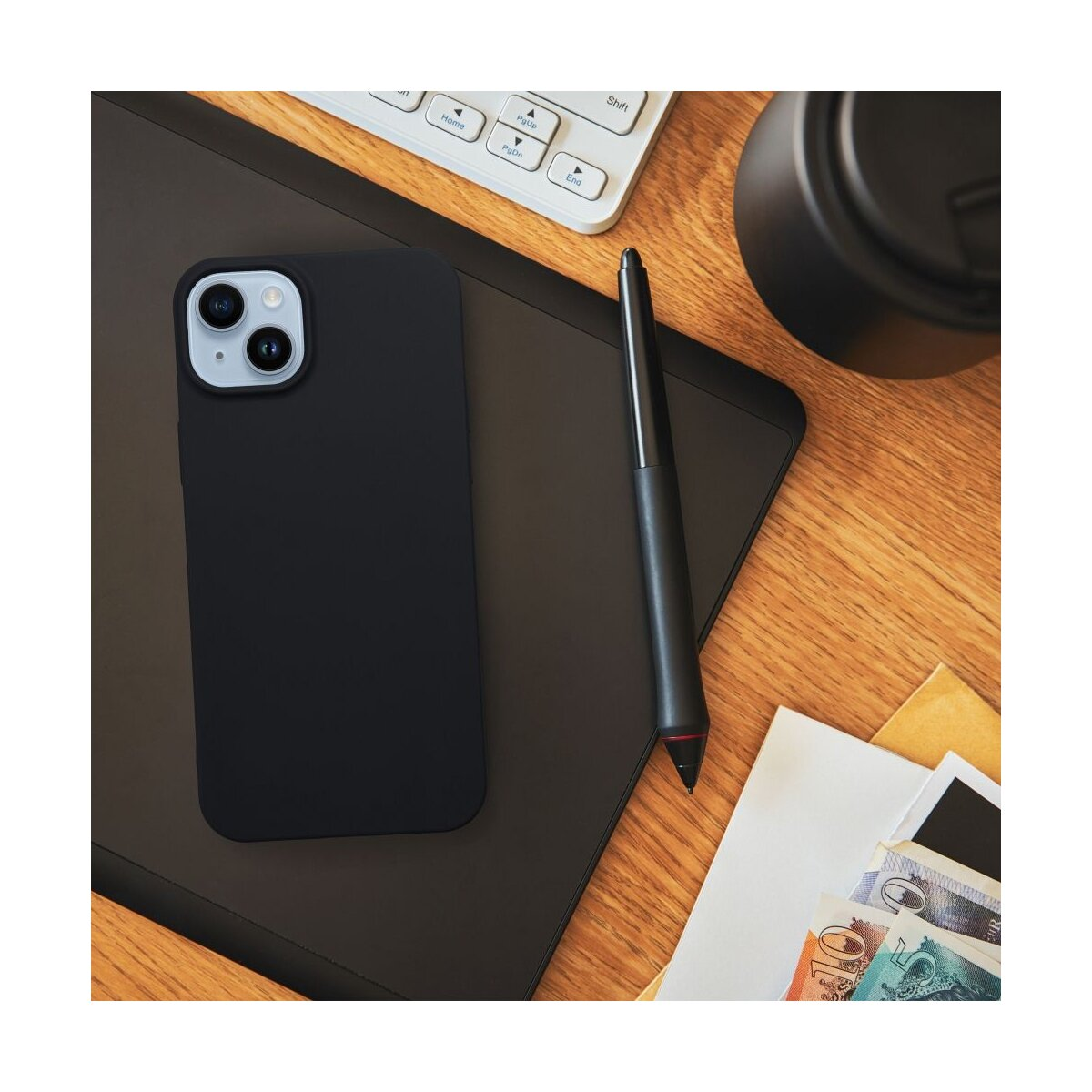 Een zwarte telefoonhoes, stylus, toetsenbord en contant geld op een houten bureau.