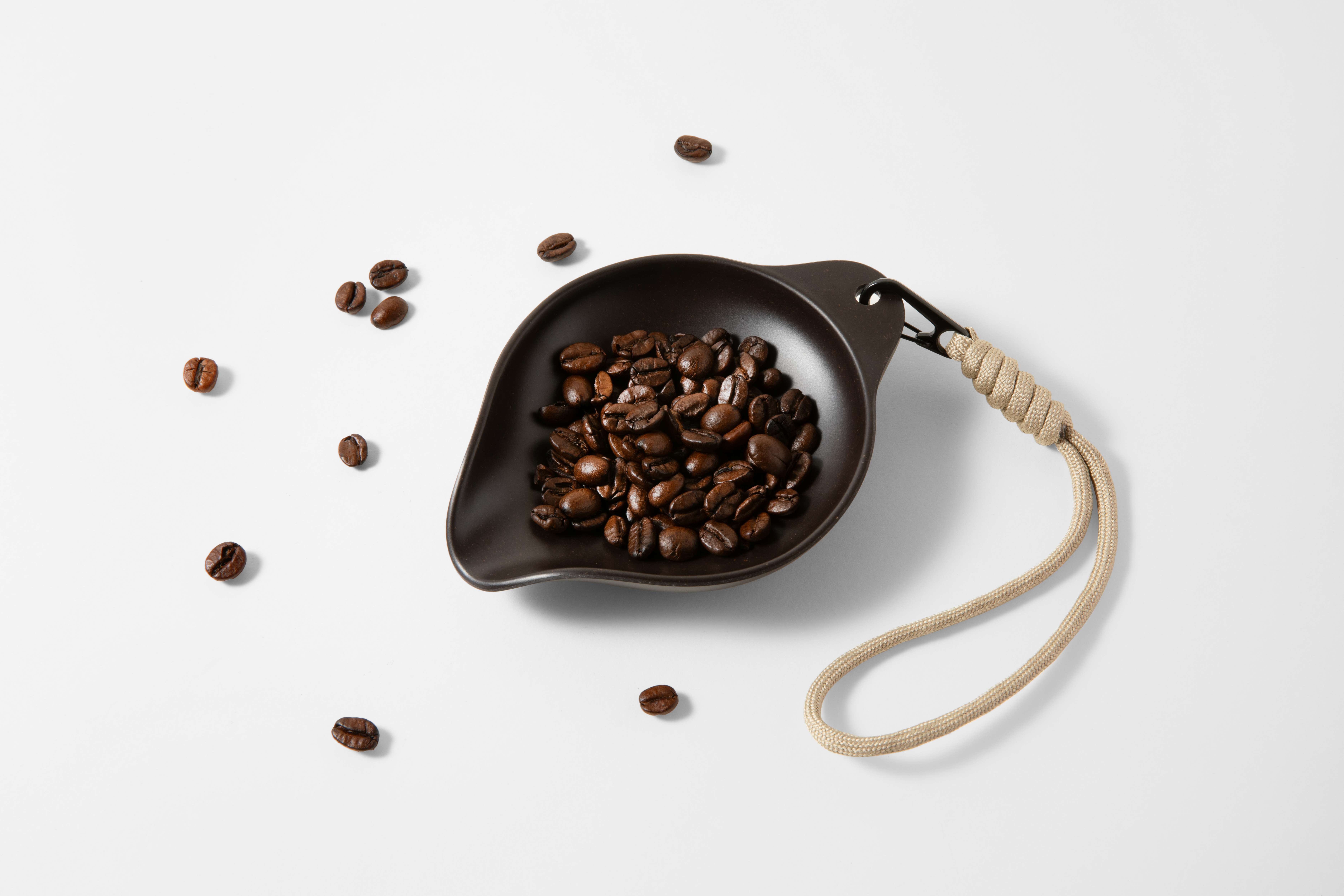 Caffè in grani scuri in una ciotola scura con corda su sfondo bianco.