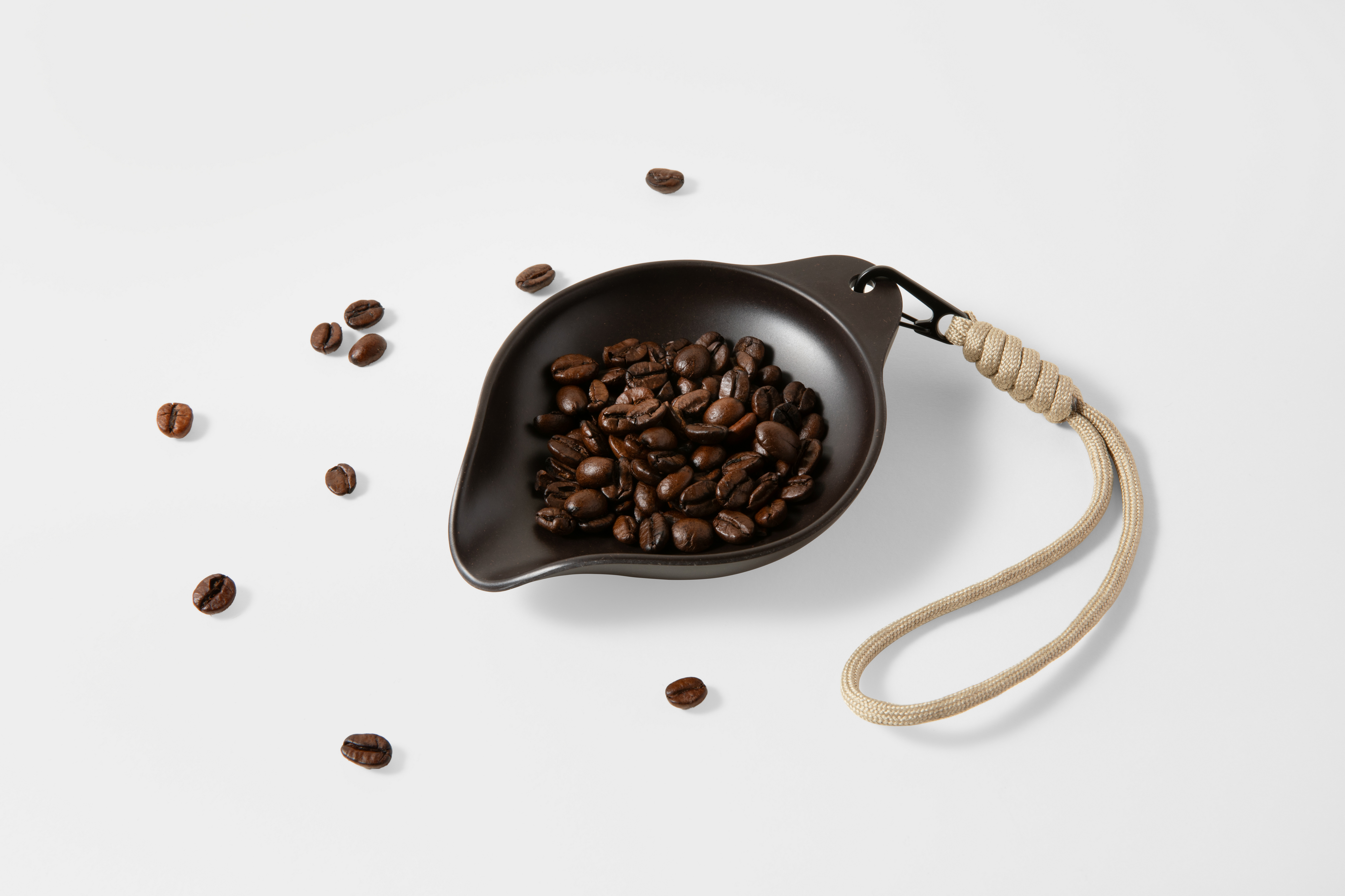 Chicchi di caffè scuro in un piatto marrone con una corda beige.